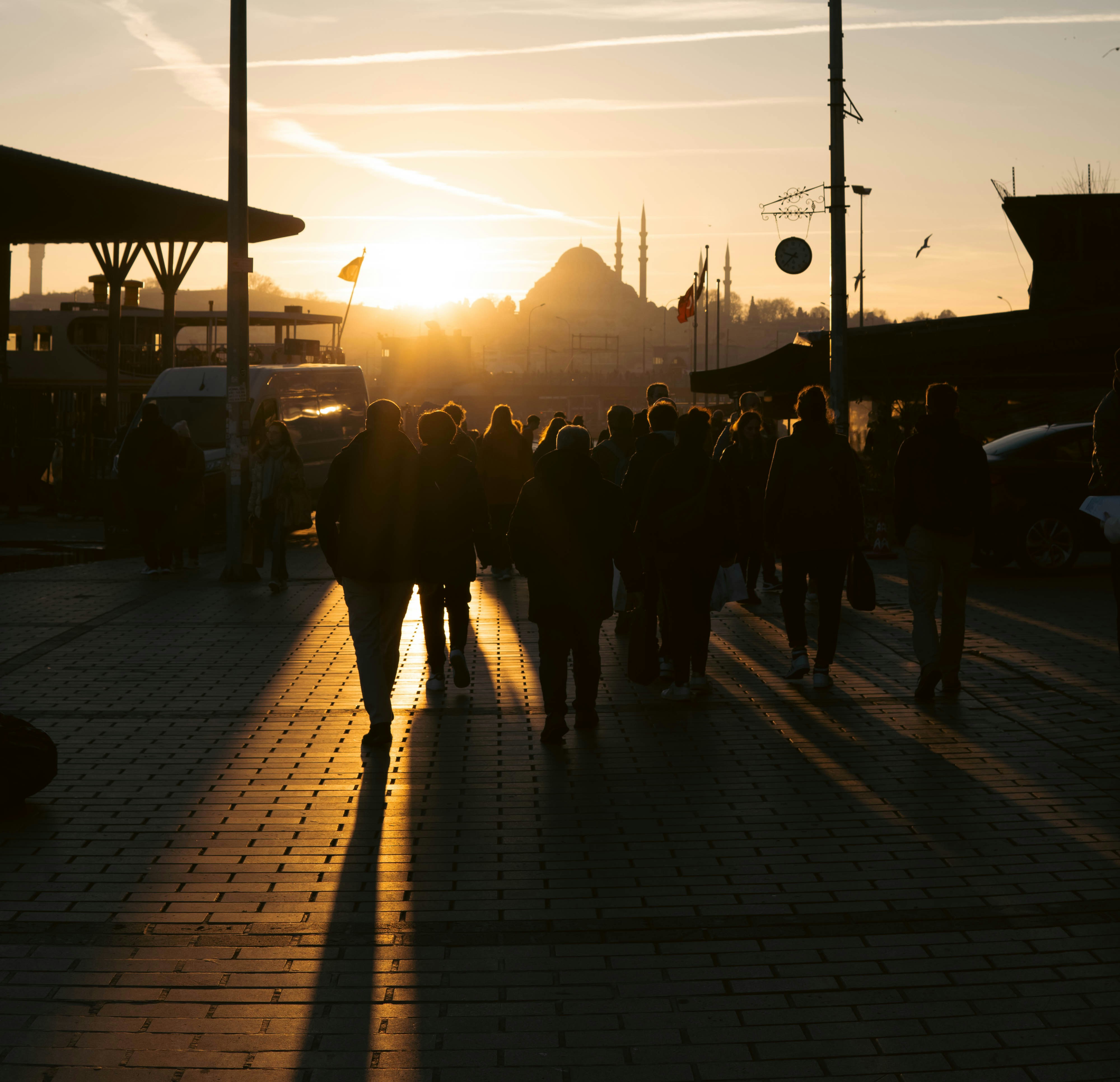 A group of people walking down a sidewalk at sunset