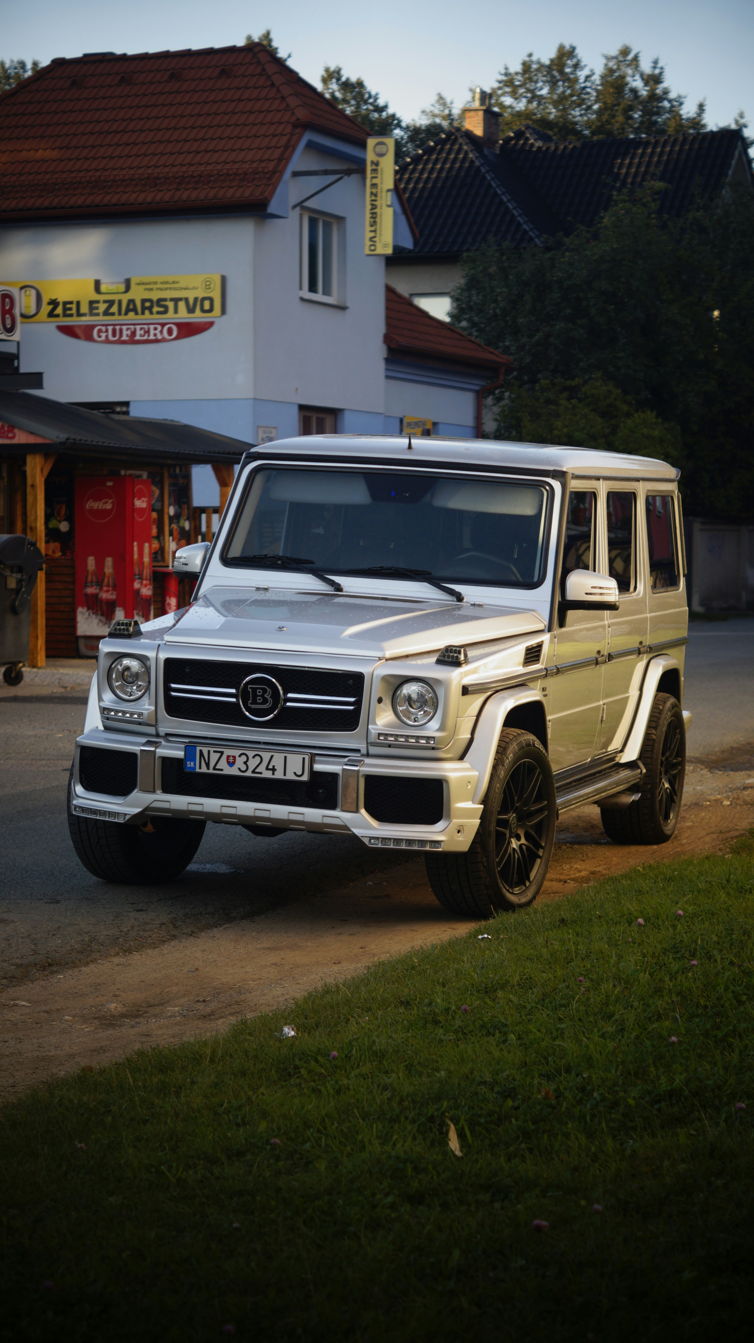 Image of a 4 door, white luxury SUV on a narrow road in what appears to be a small town, perhaps in Europe