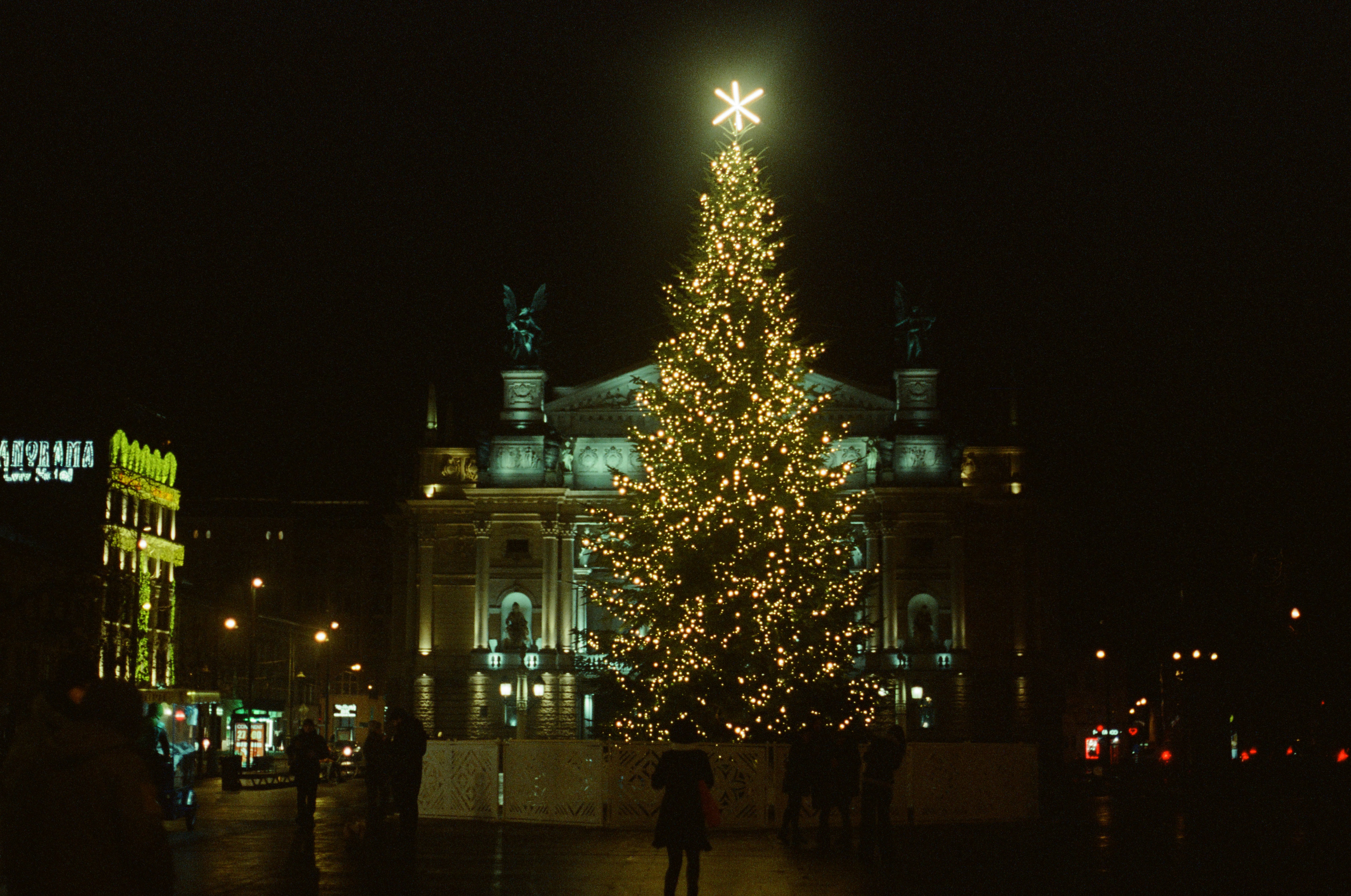 A lit christmas tree in front of a large building