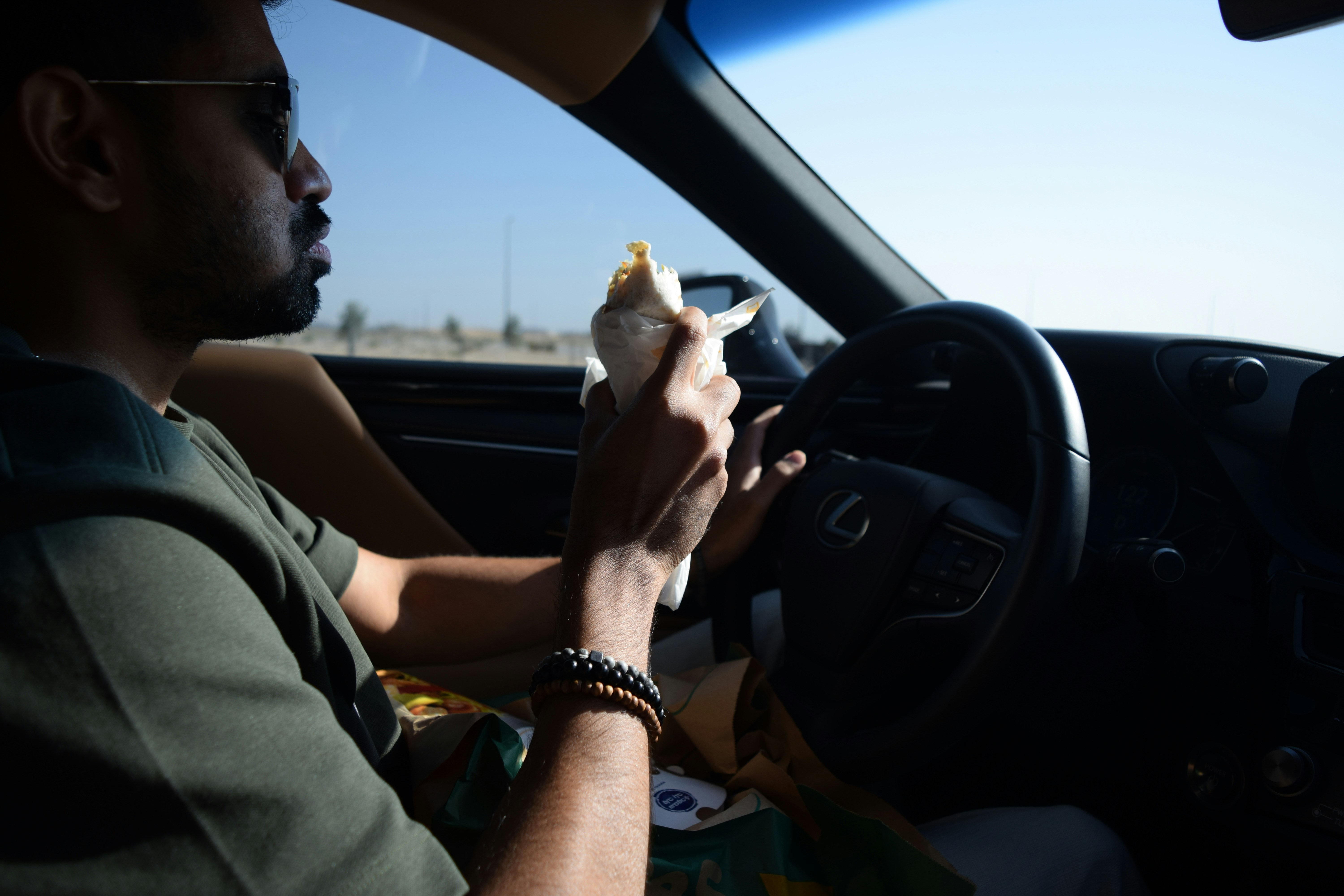 A man driving a car while holding a hot dog