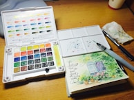 A wooden table topped with a white box filled with watercolors