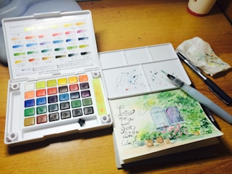 A wooden table topped with a white box filled with watercolors