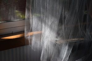 A cat sitting on a window sill in front of a curtain