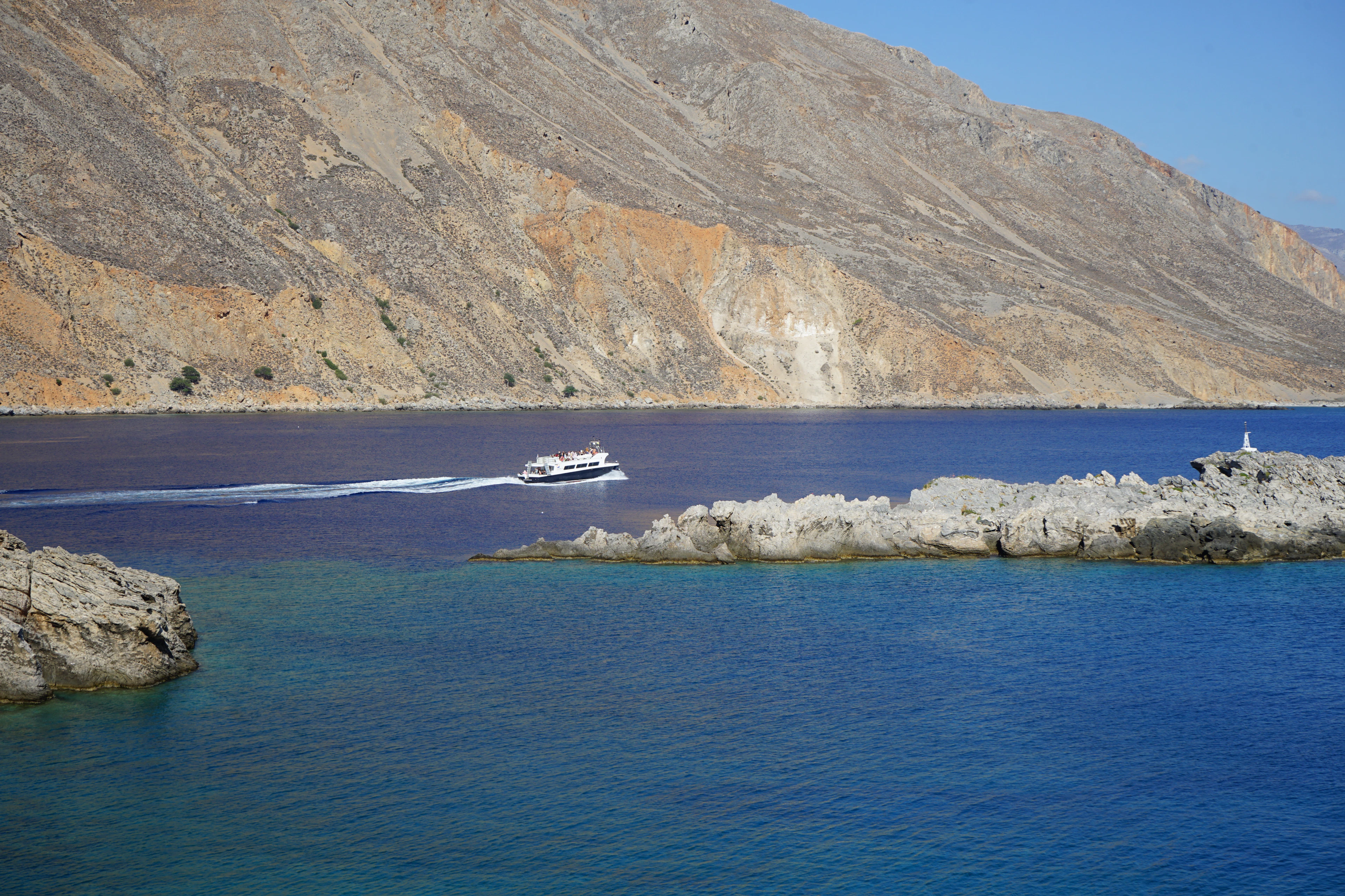 A small ferry crosses a turquoise bay below rugged bare mountains near Loutro, Crete.