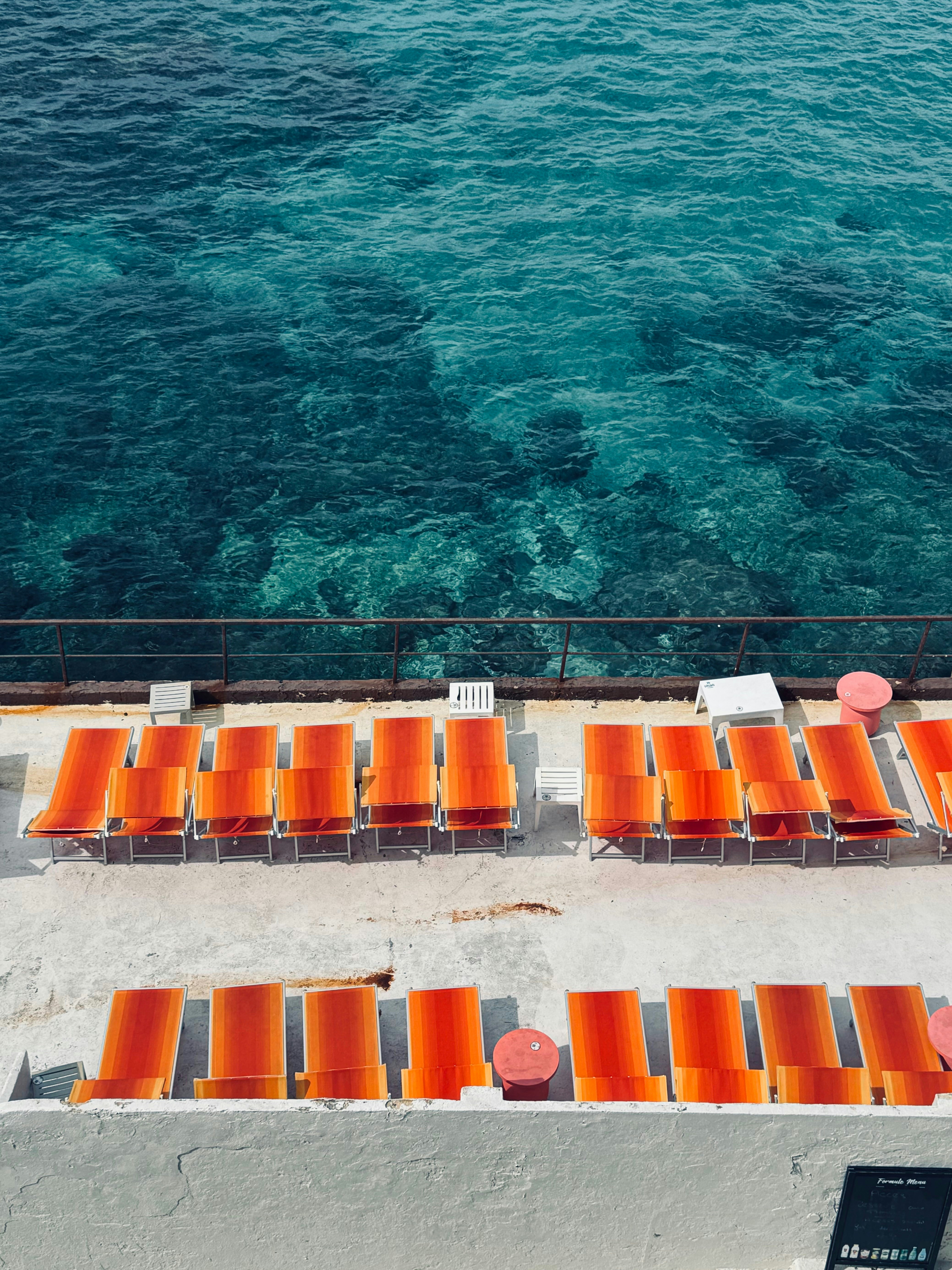 A group of orange chairs sitting next to a body of water