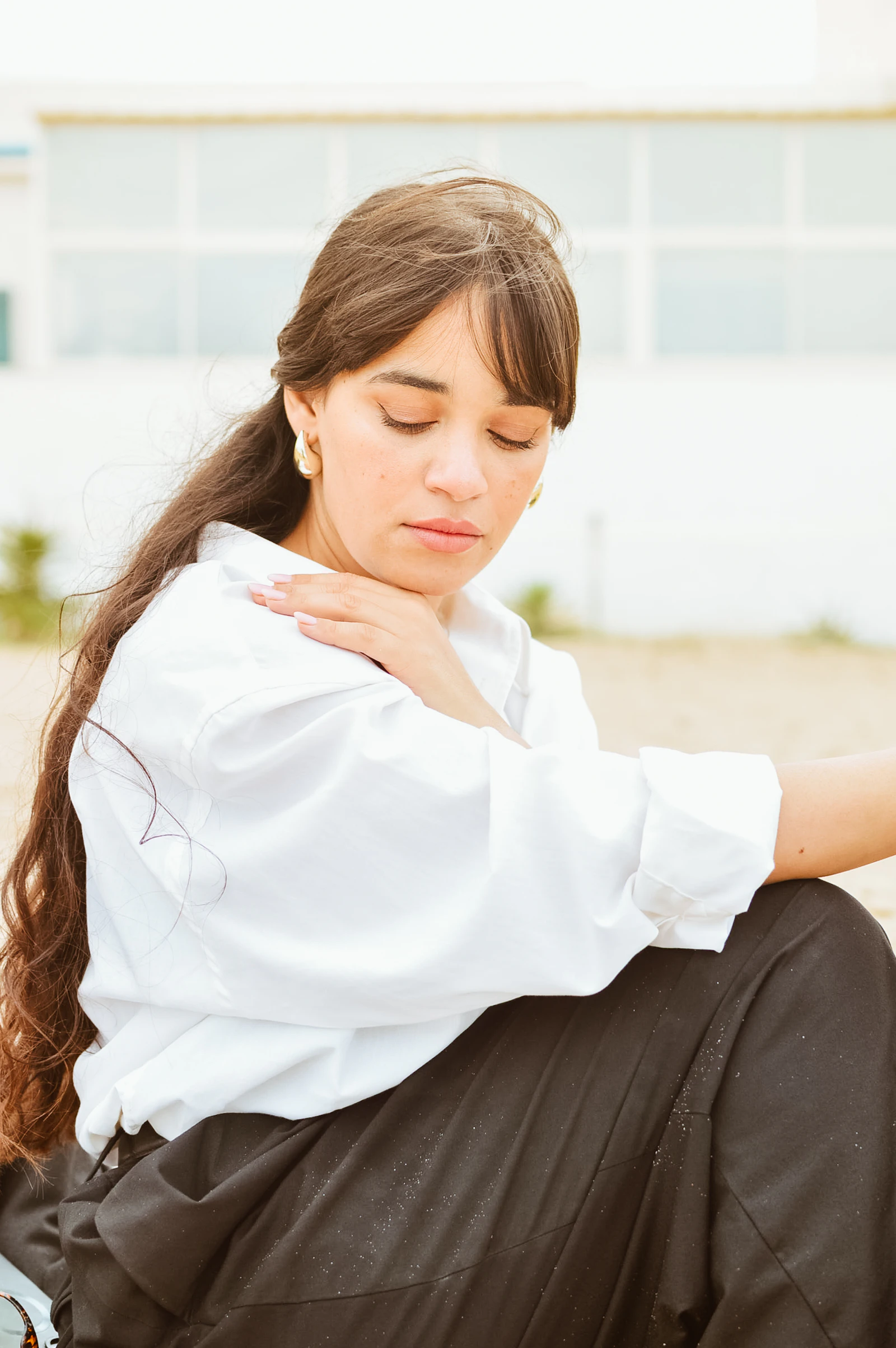 A woman sitting with her hand resting on her shoulder, eyes closed