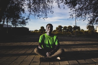 A man in a green shirt sitting on a wooden floor