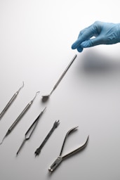 A hand in a blue glove is pointing at a set of surgical instruments
