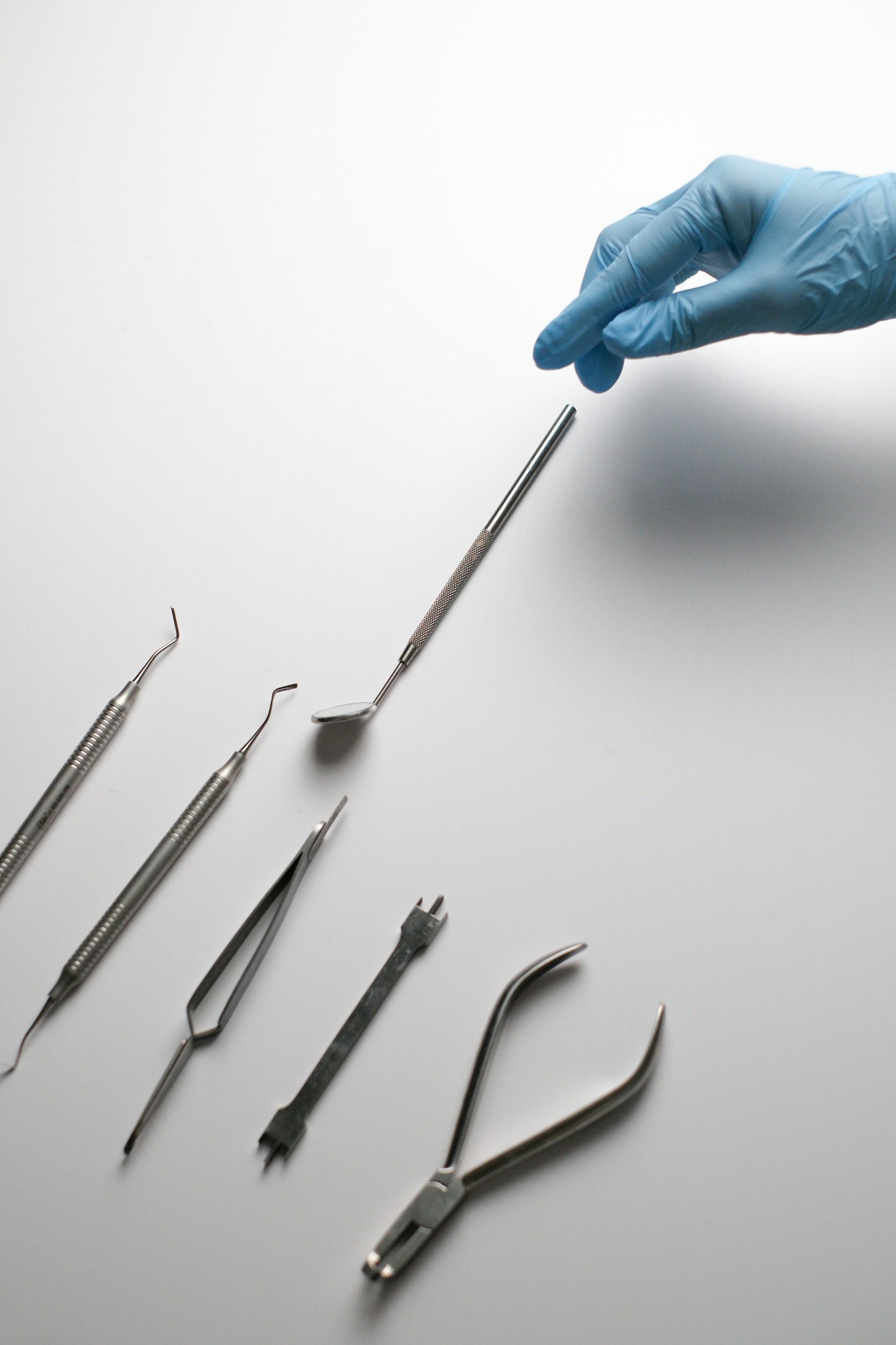A hand in a blue glove is pointing at a set of surgical instruments