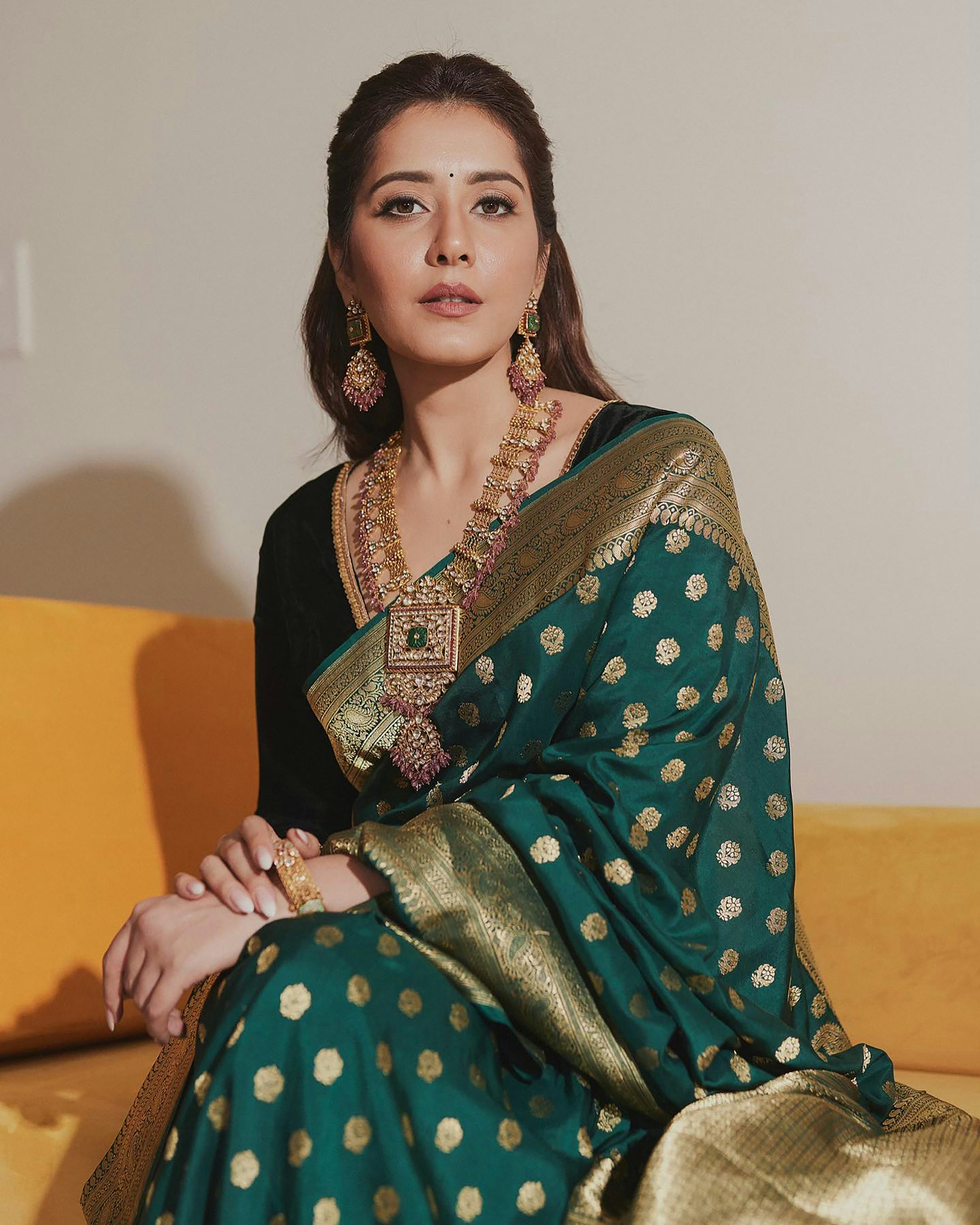 A woman sitting on a couch wearing a green and gold sari