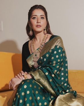 A woman sitting on a couch wearing a green and gold sari