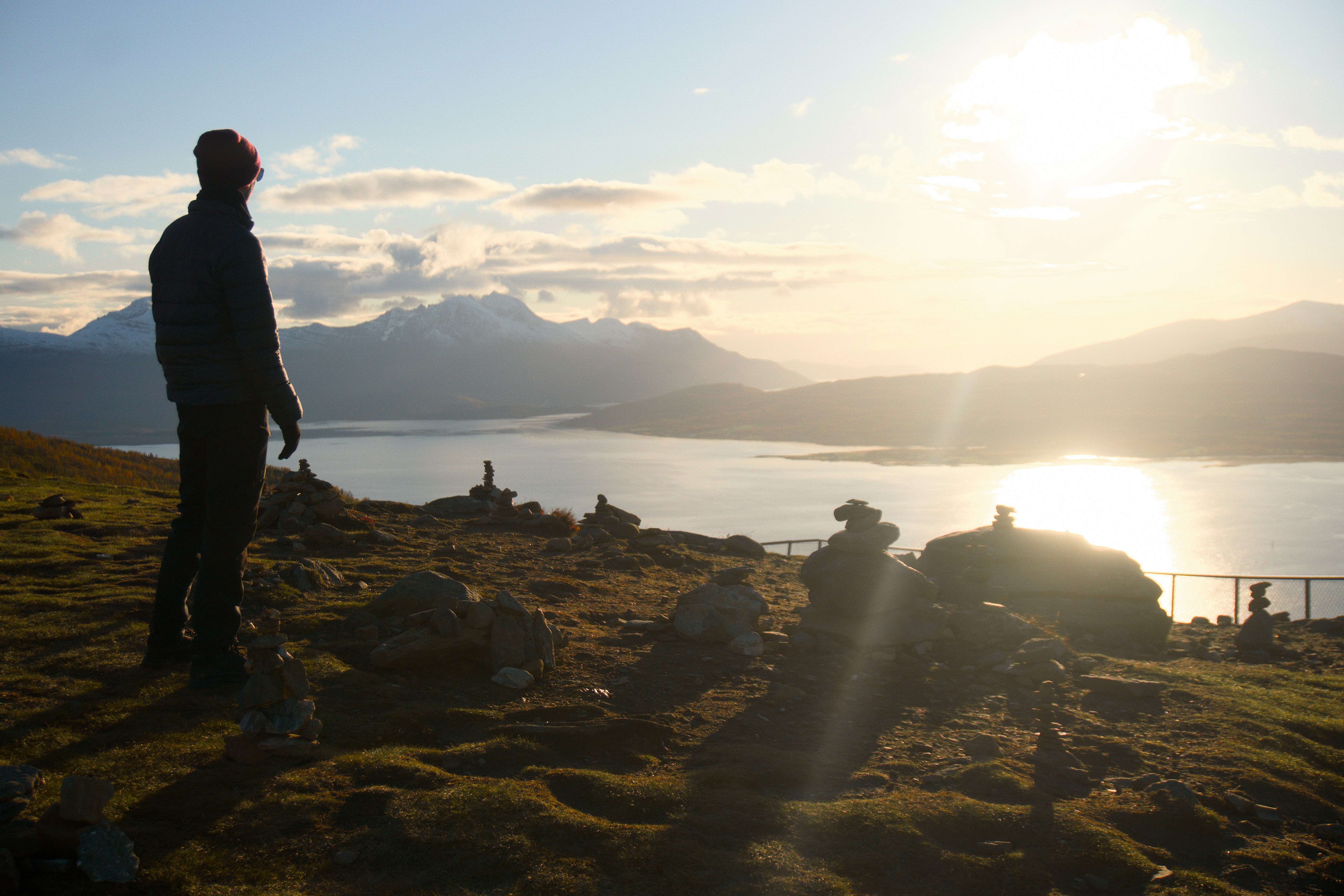 Person i dunjakke ser ud over gylden fjord med snedækkede bjerge.