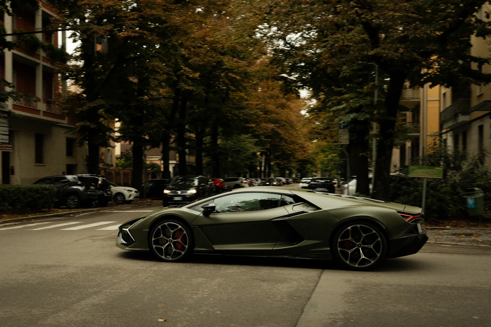 Olive green Lamborghini Revuelto on a tree-lined street