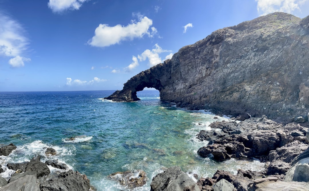 A rocky beach with a large rock arch in the middle of it,