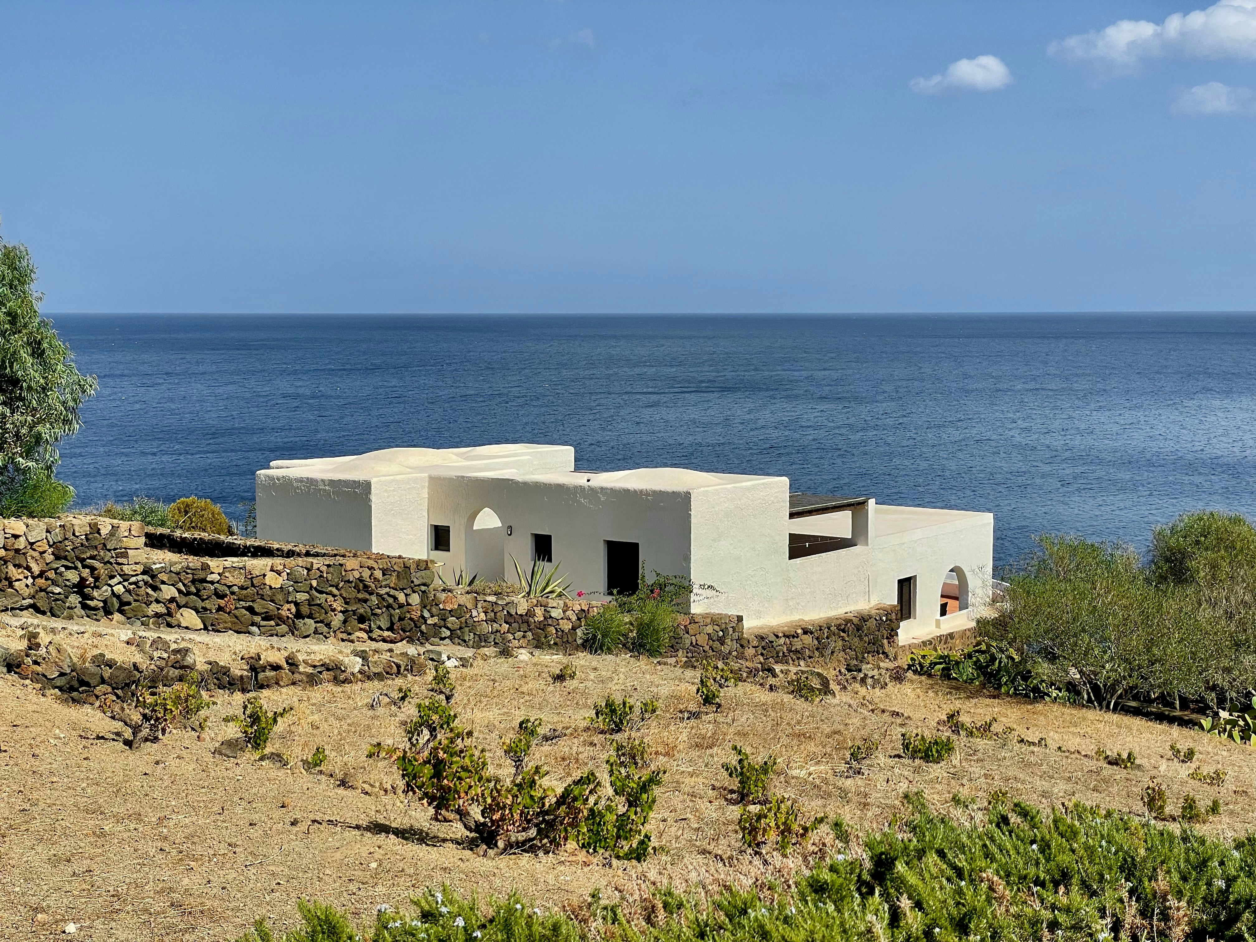 A white house sitting on top of a hill next to the ocean, 