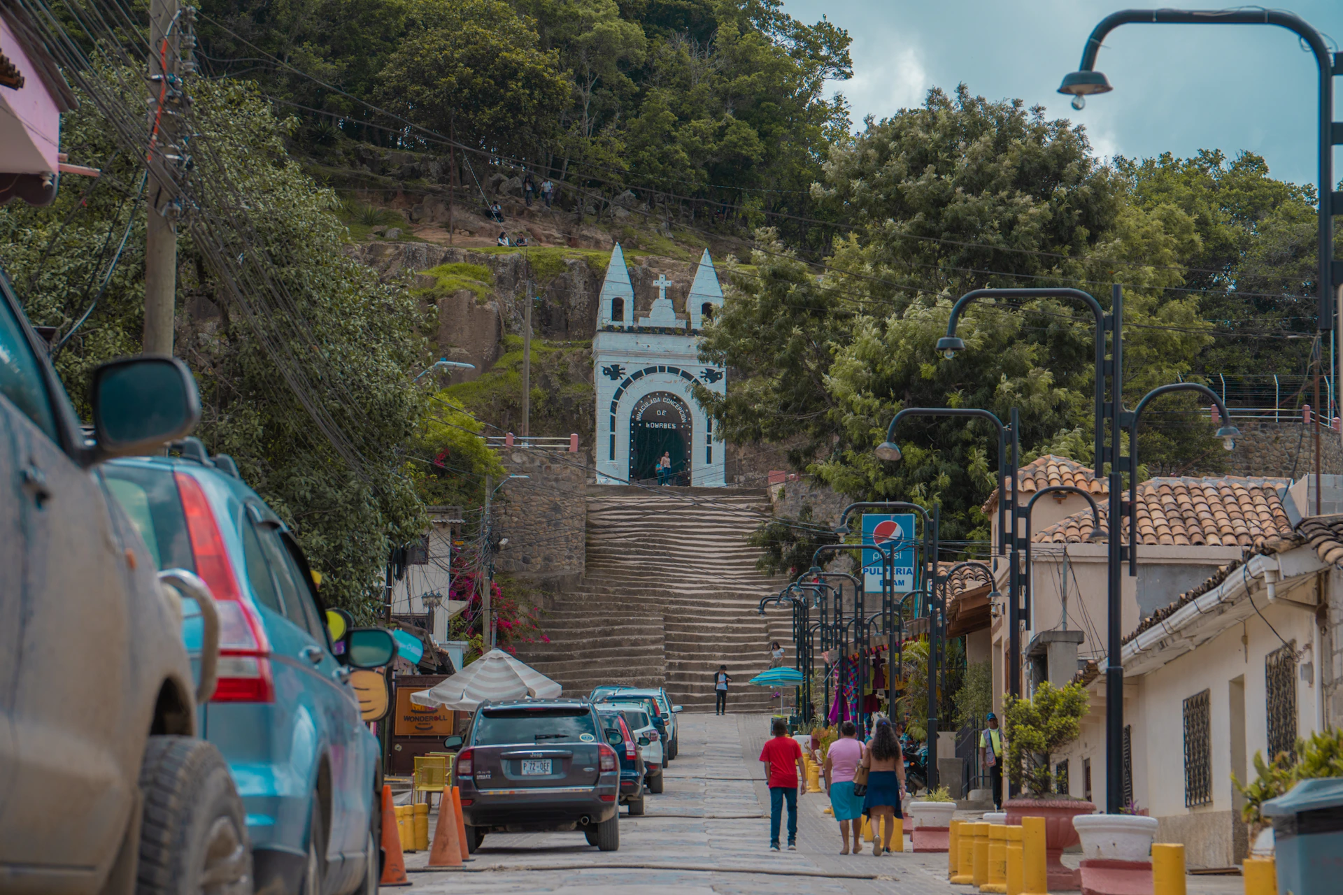 A group of people walking down a street next to parked cars