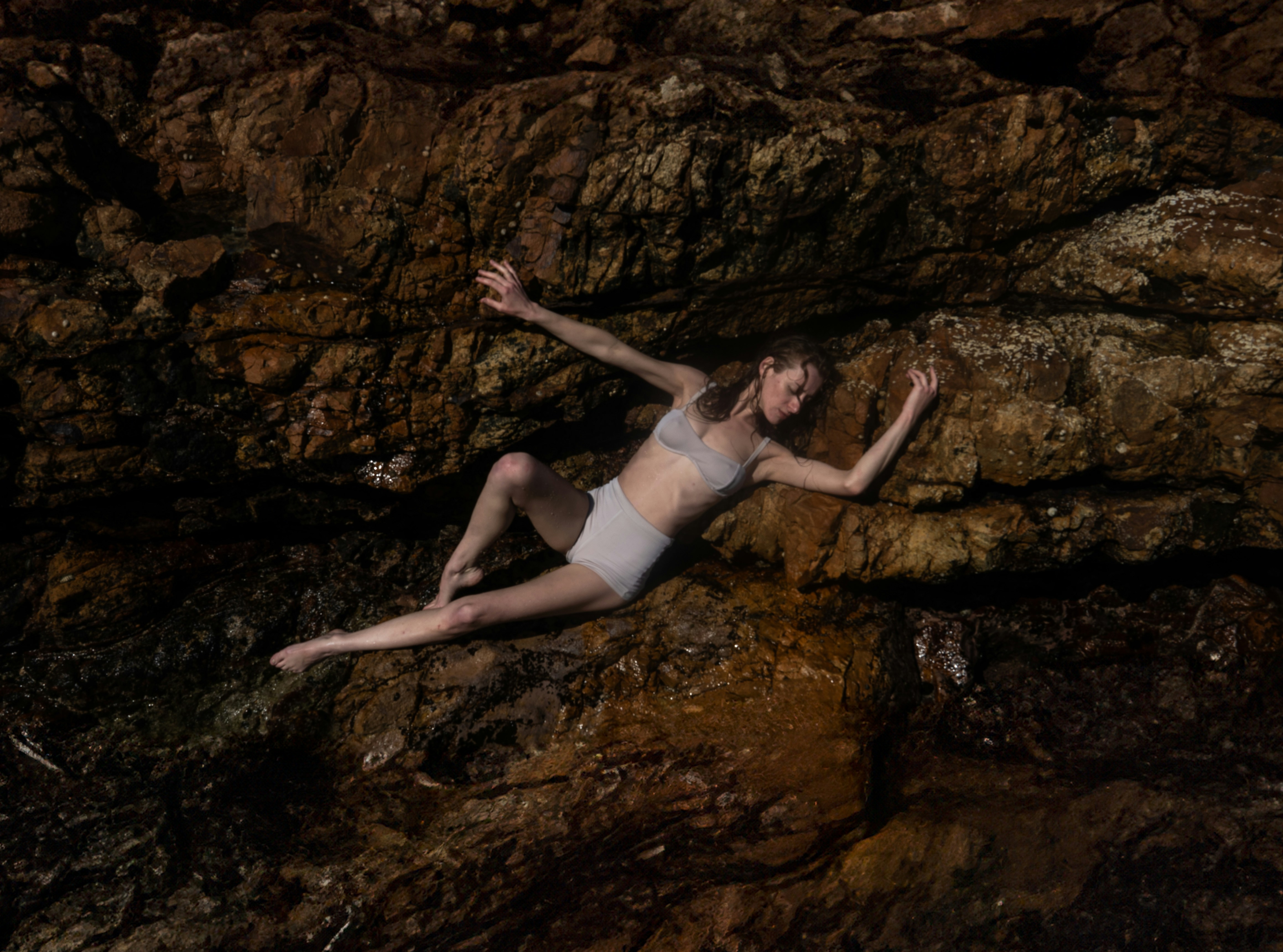 A man laying on top of a rock next to a body of water