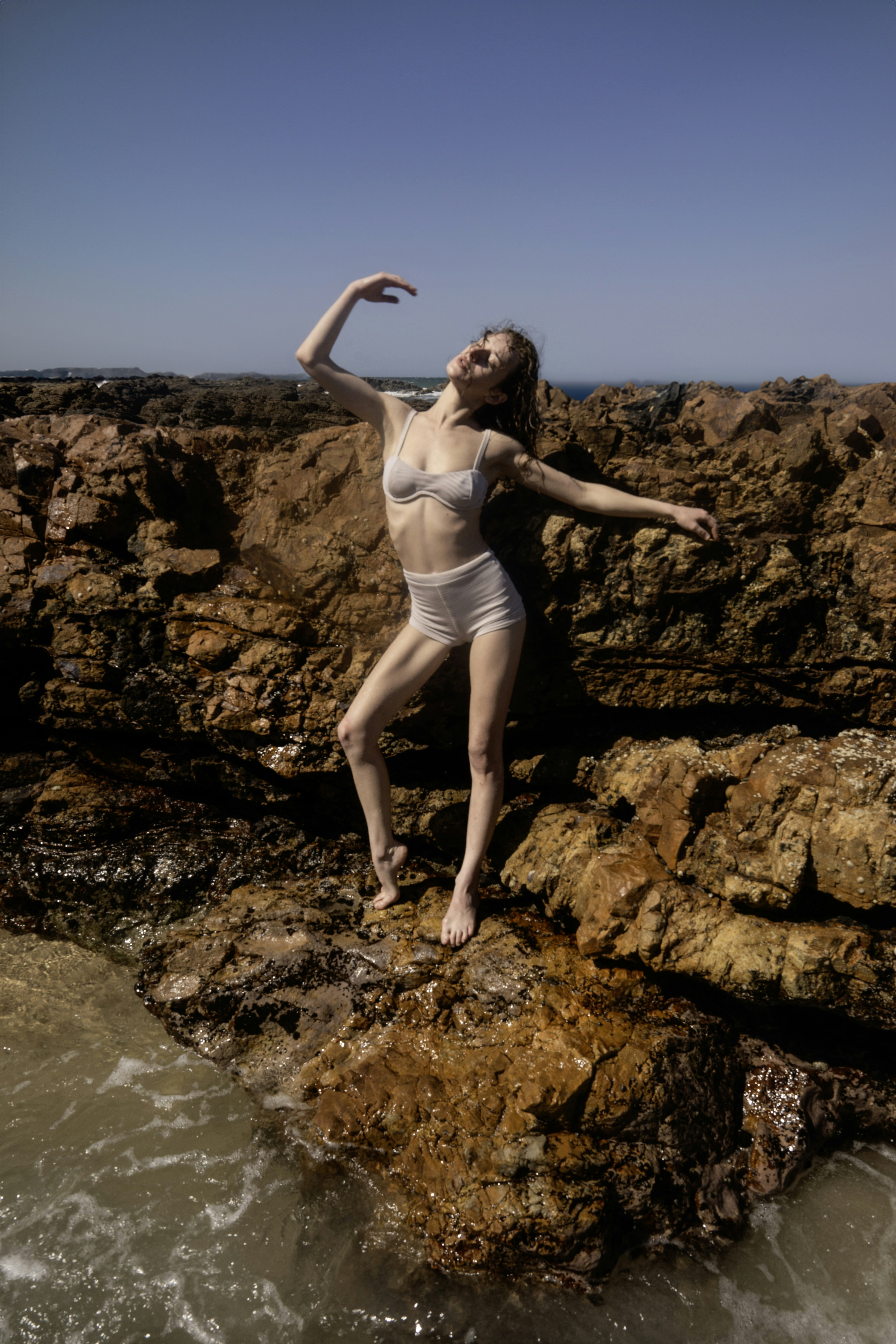 A woman in a white bikini standing on a rock by the ocean