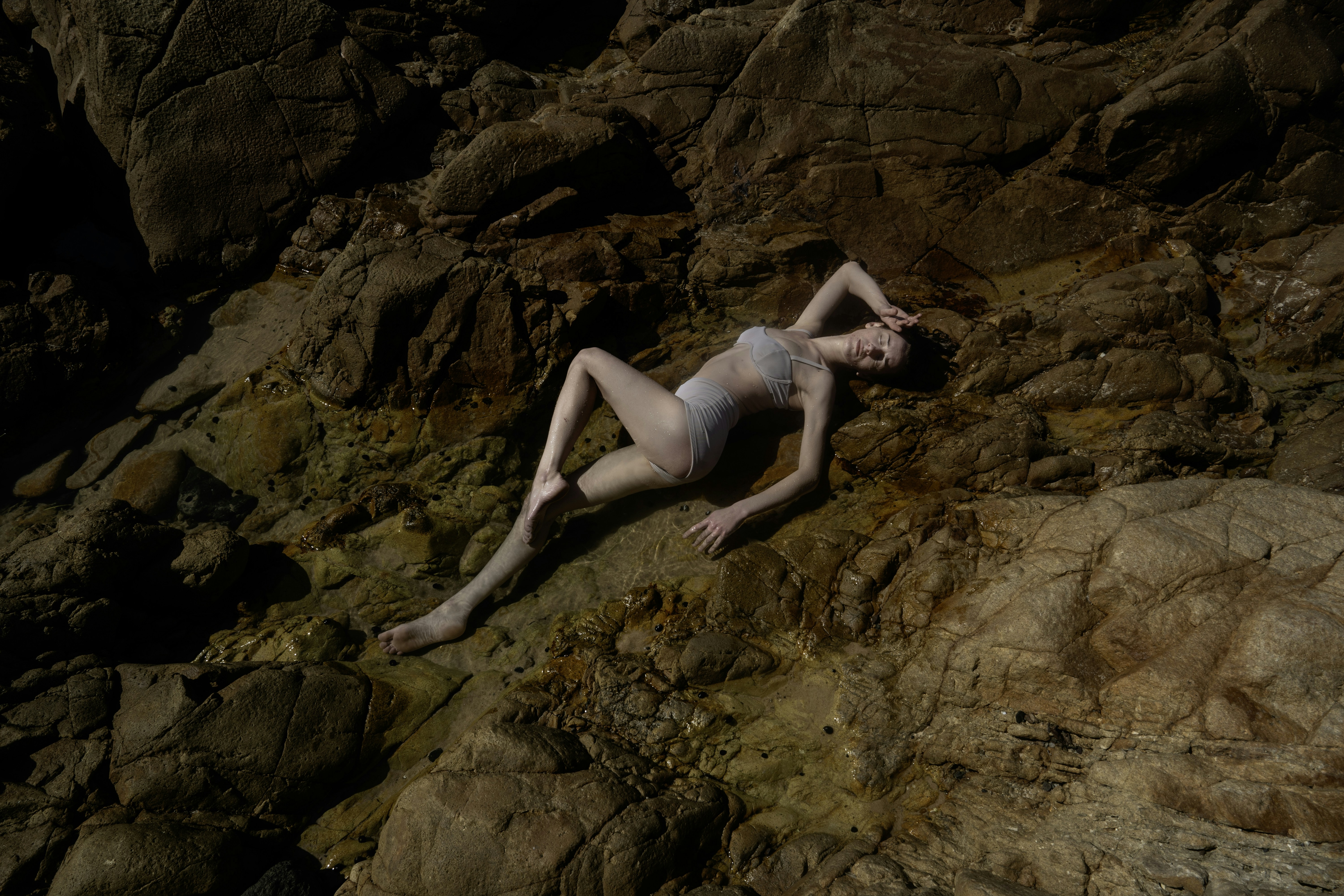 A naked woman laying on top of a rocky cliff