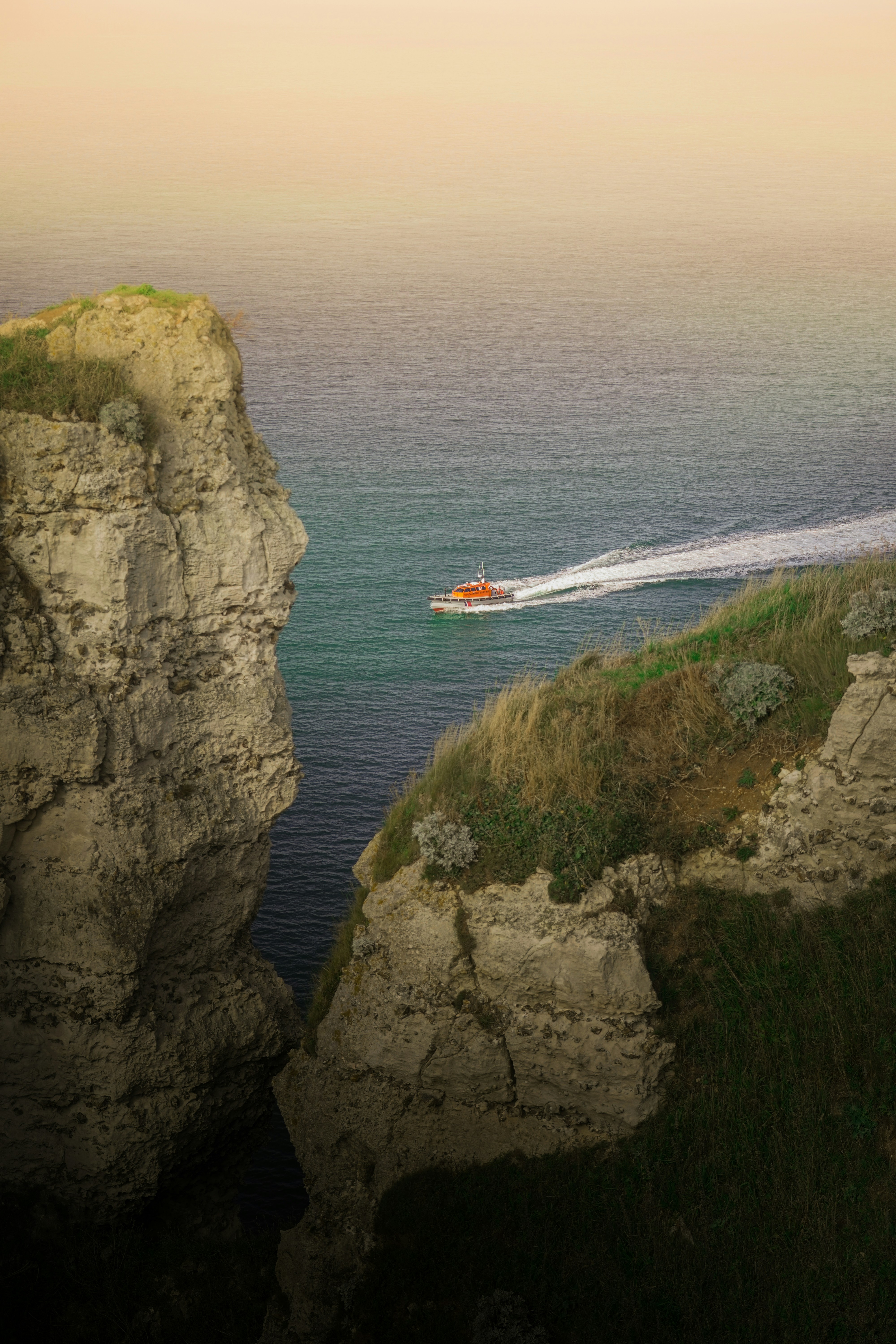 A boat is traveling through the water near a cliff