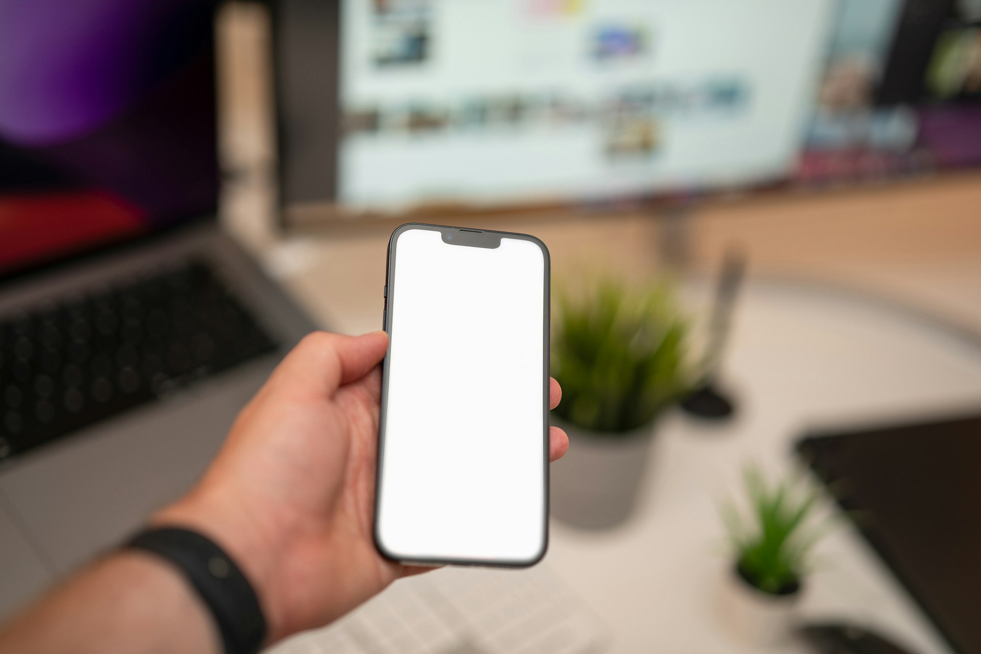 A person holding a cell phone in front of a computer