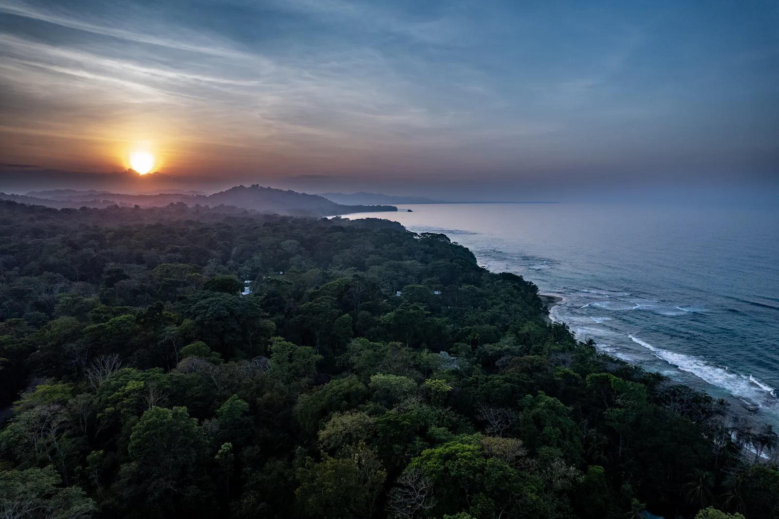 Vista aérea de la selva tropical descendiendo hasta el mar al atardecer