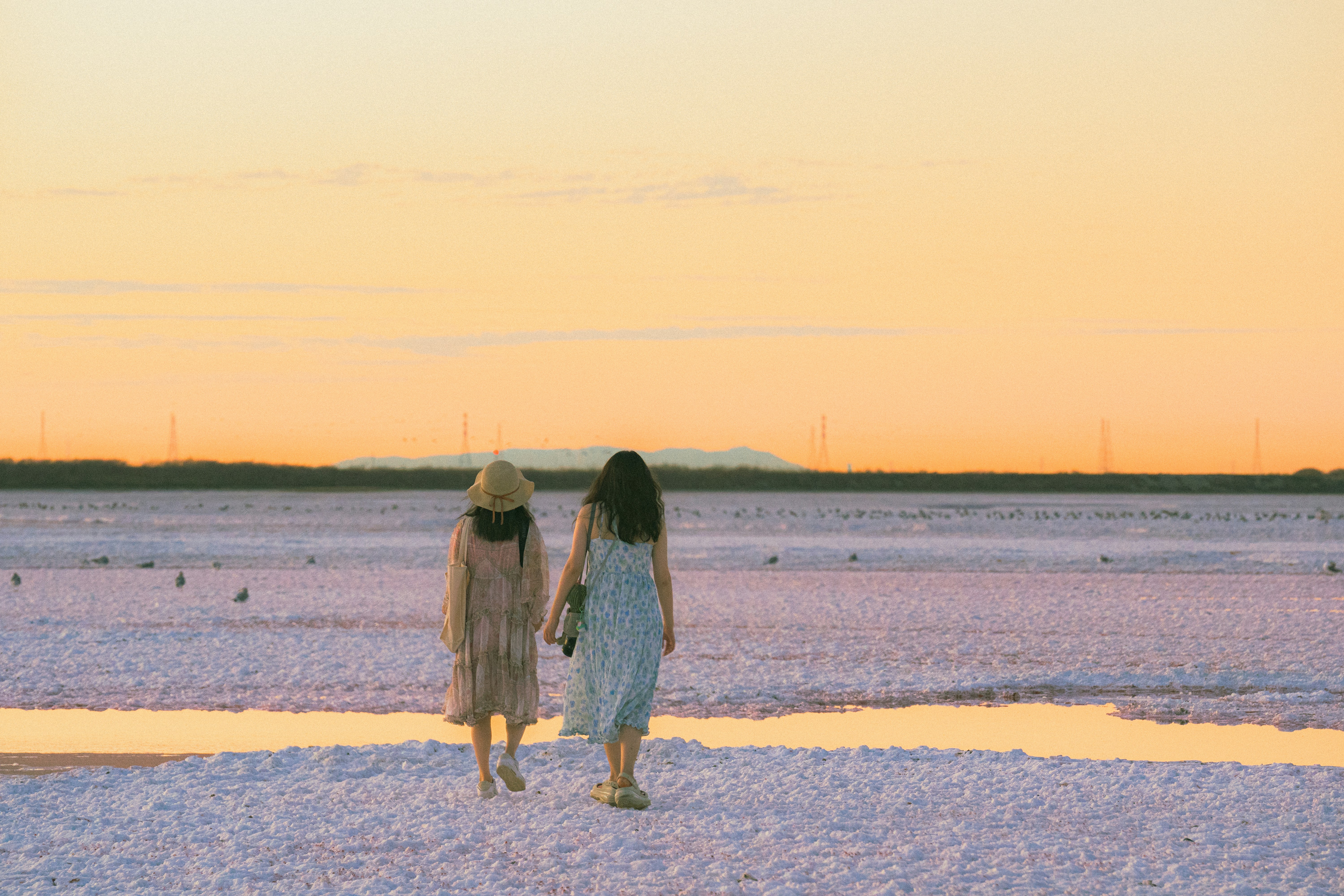 Two women walking on a beach at sunset