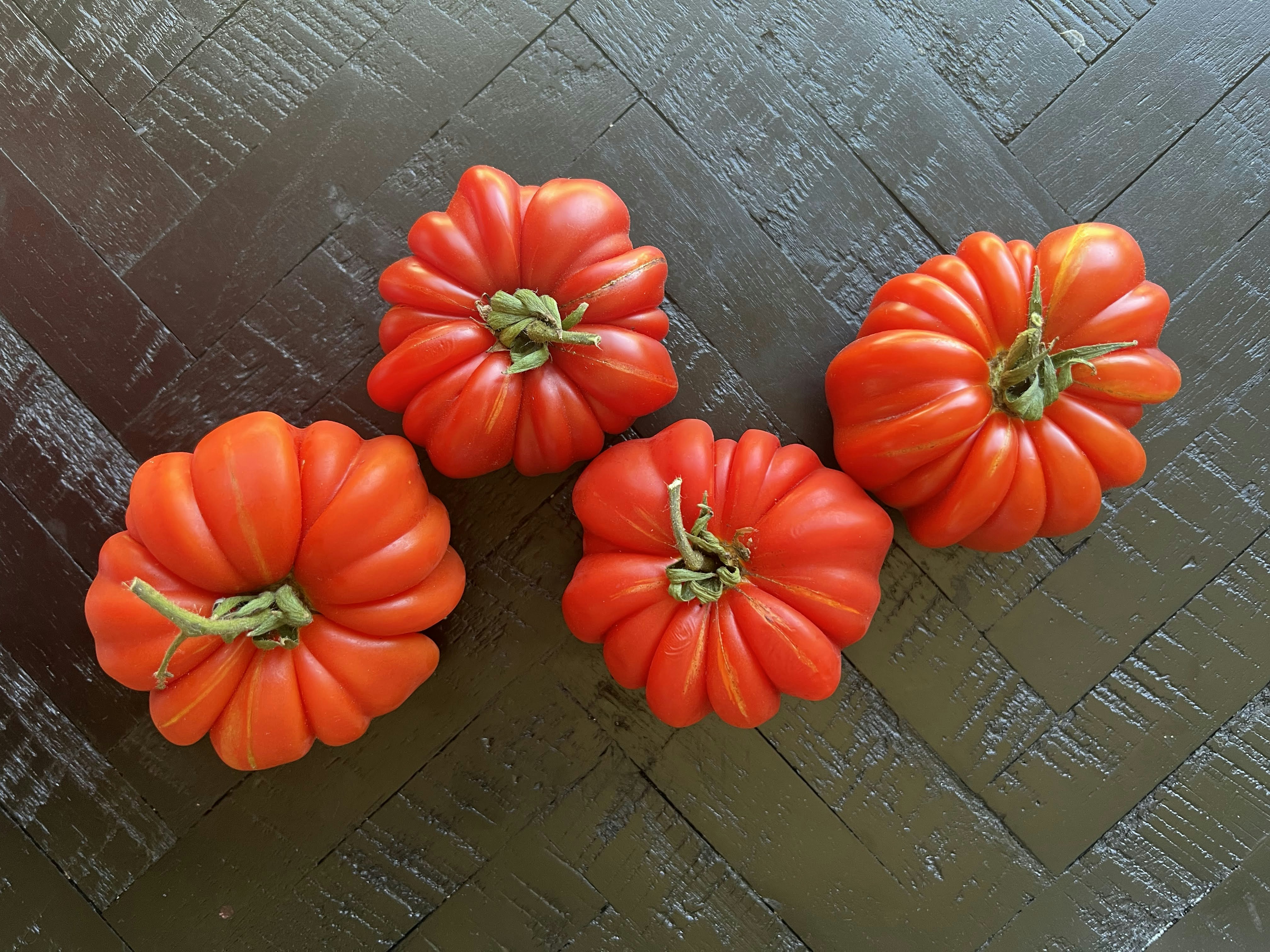 Deep red Cherokee Purple heirloom tomatoes on a rustic wooden board with garden soil