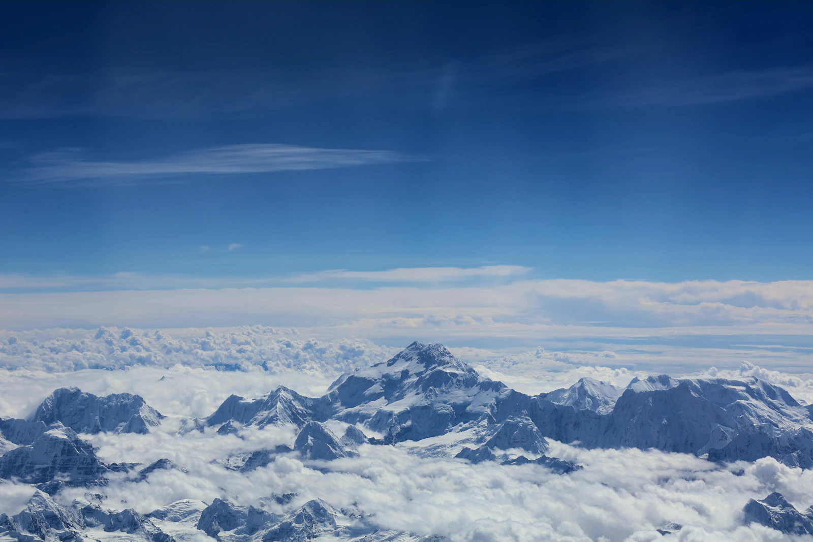 Everest's dark summit pyramid rising above a sea of cloud and the snowy Himalaya, seen from an aircraft window