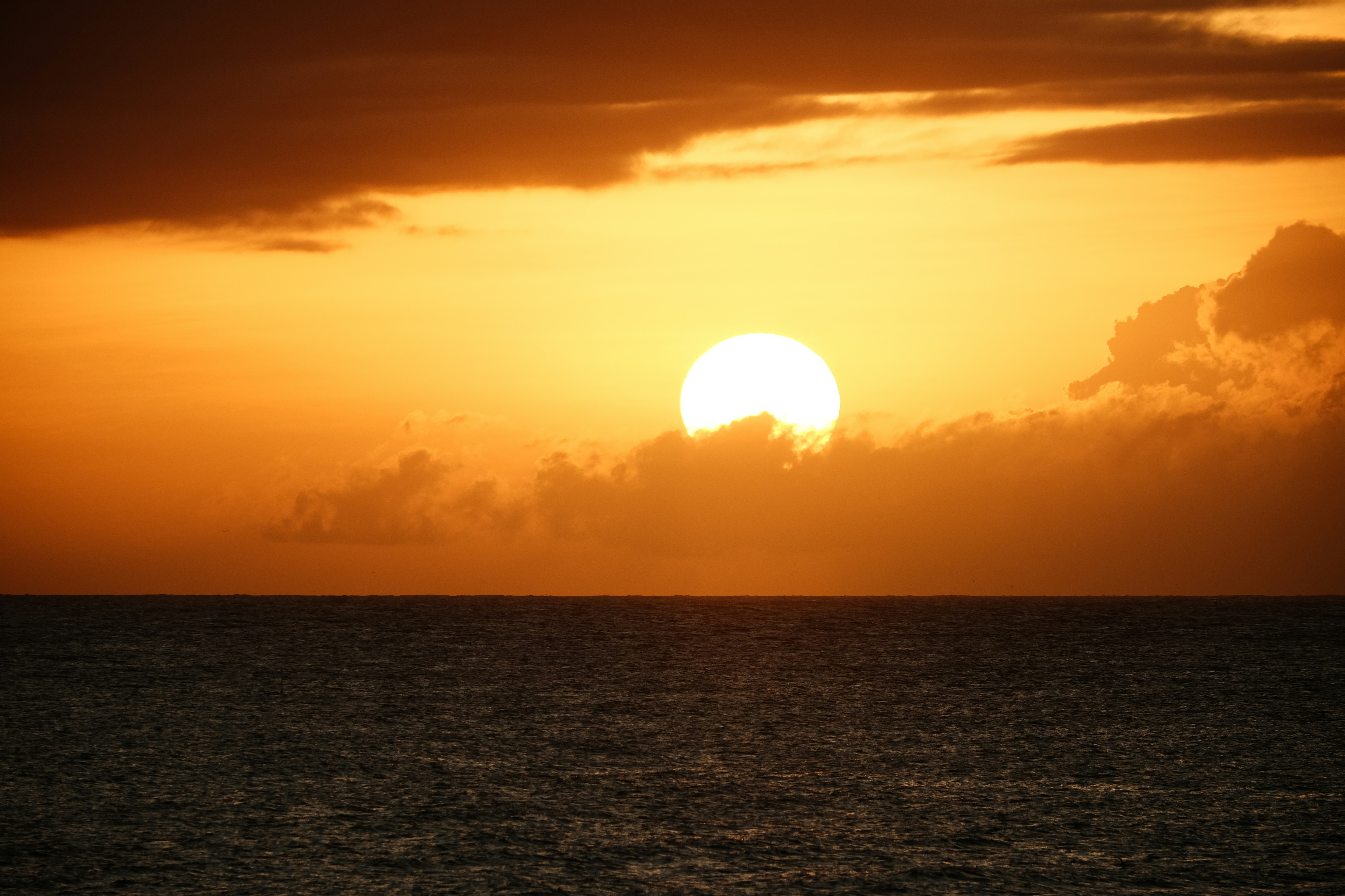 The sun is setting over the ocean on a cloudy day