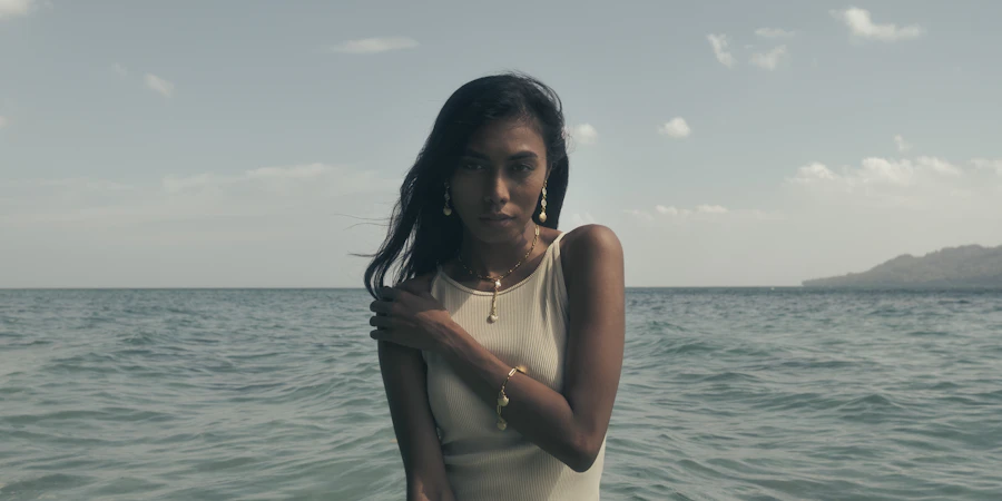Adult woman standing in turquoise water wearing gold jewelry on a breezy day