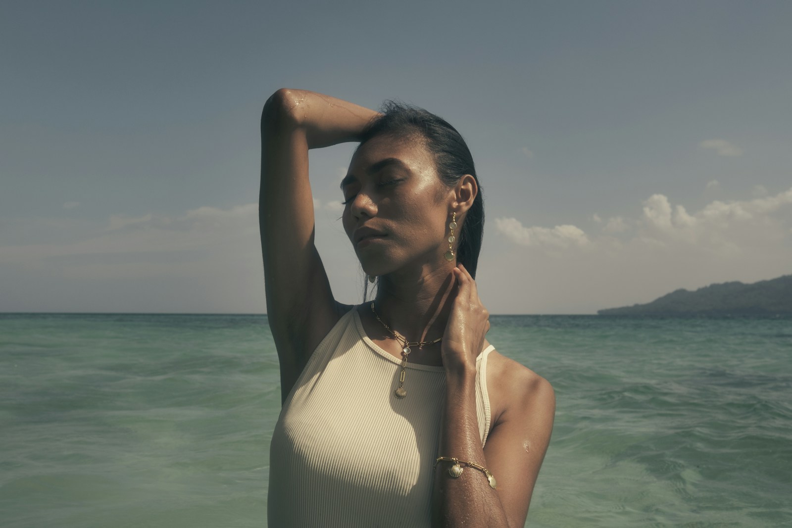 Mulher de top branco dentro do mar com os braços para trás