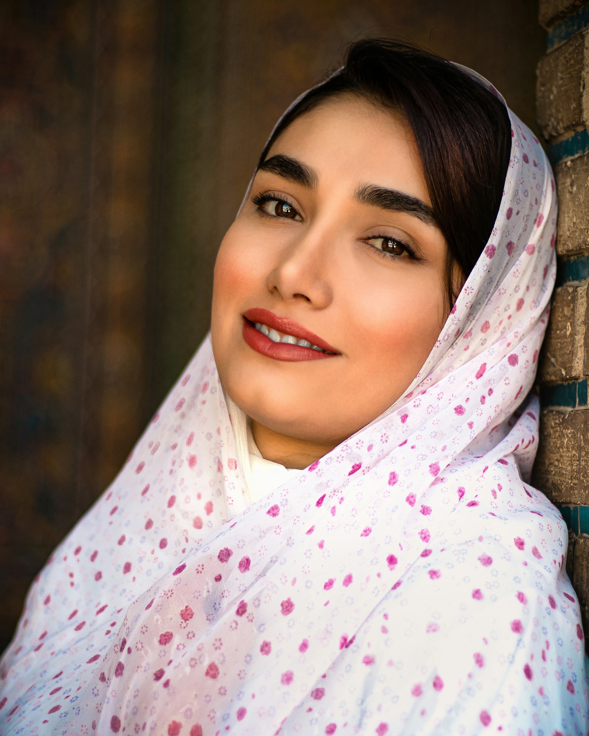 A woman in a headscarf leaning against a brick wall