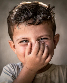 A young boy covers his face with his hands
