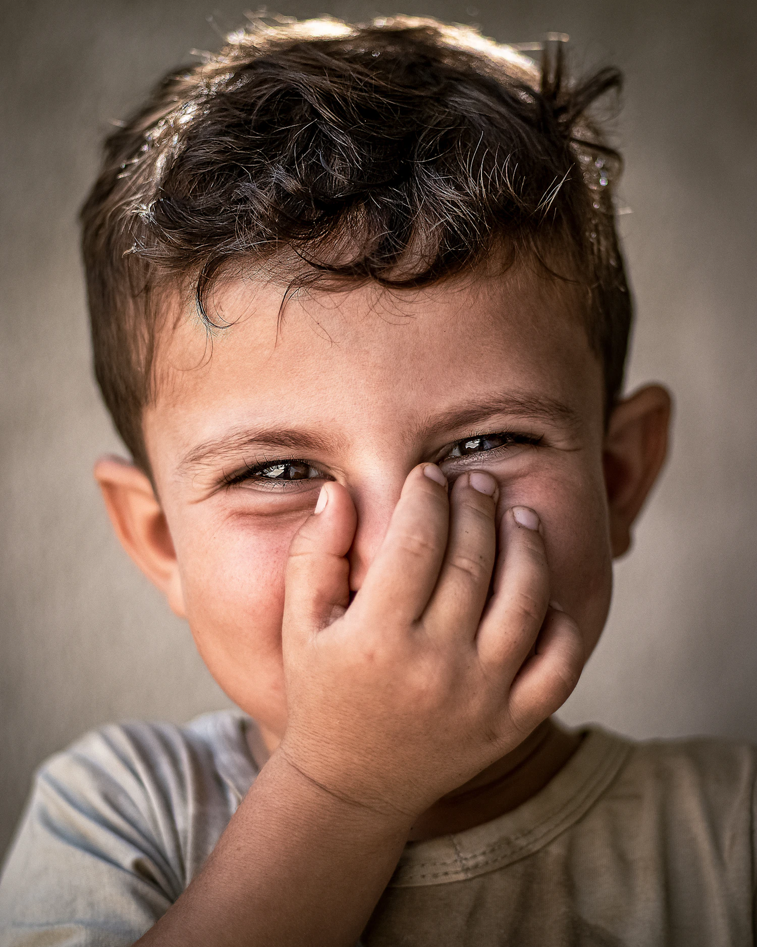 A young boy covering his face with his hands, looking nervous
