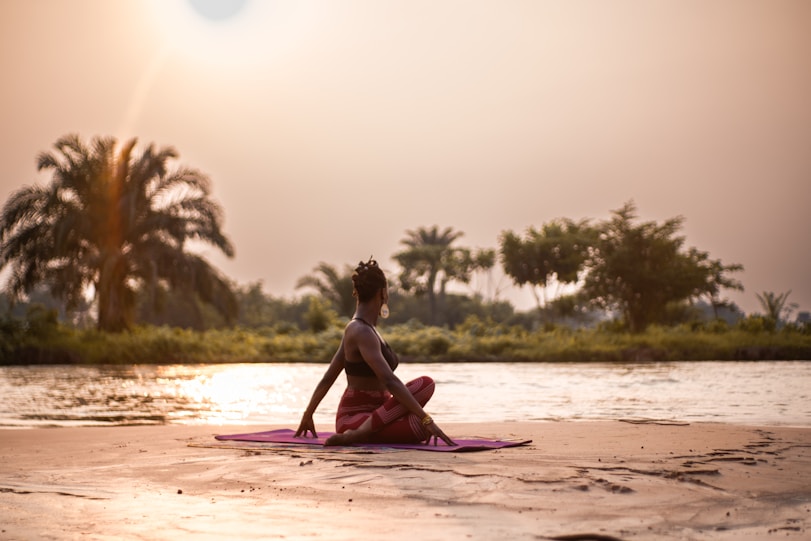 A woman sitting on a pink mat on a river bank