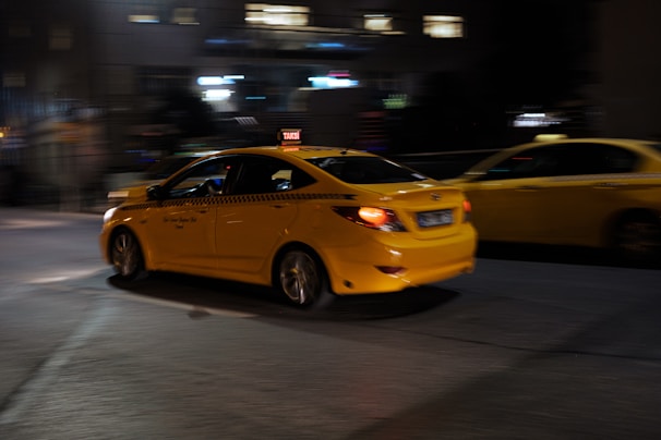 A yellow car driving down a street at night