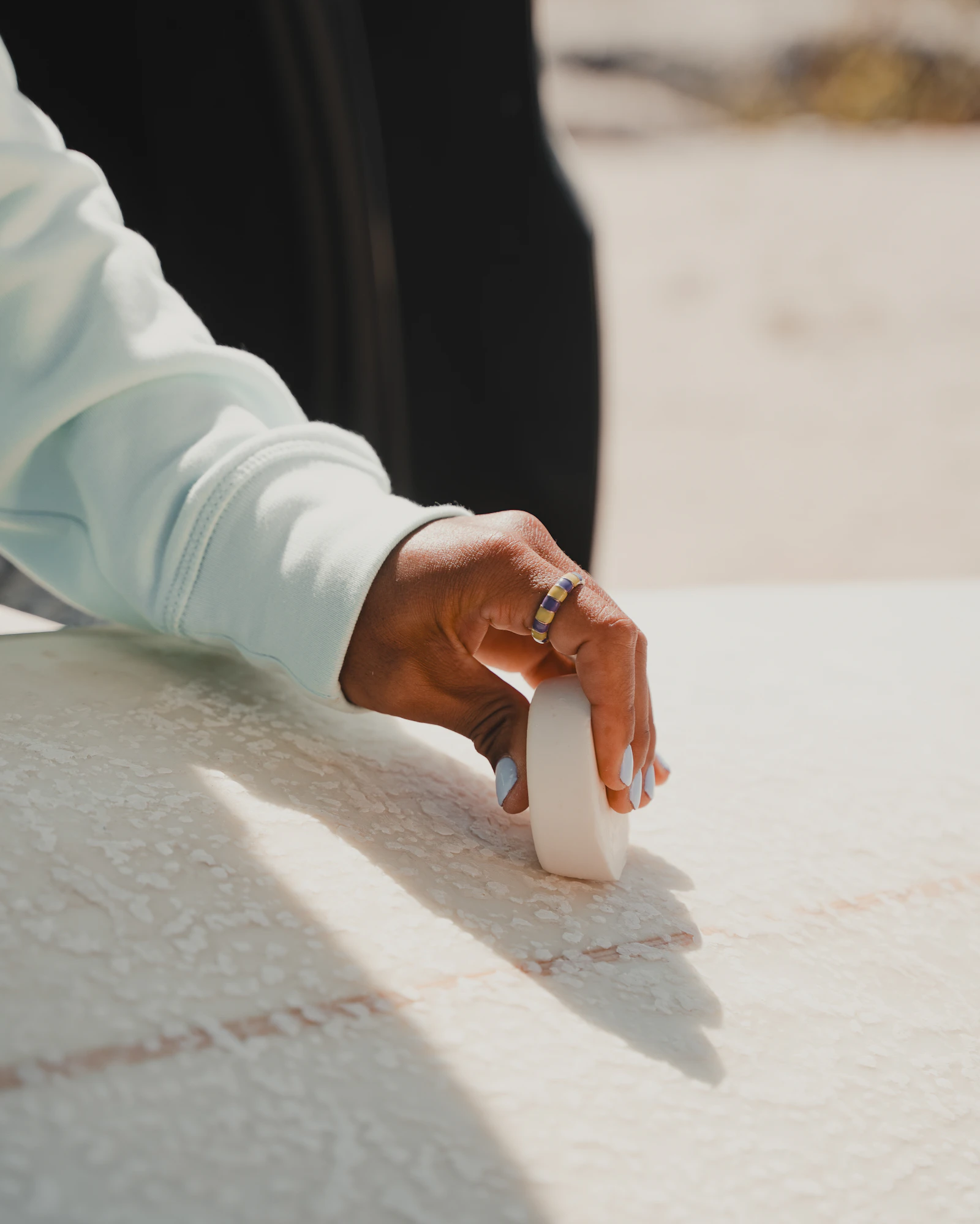 A hand pressing a bar of wax onto a pale board deck