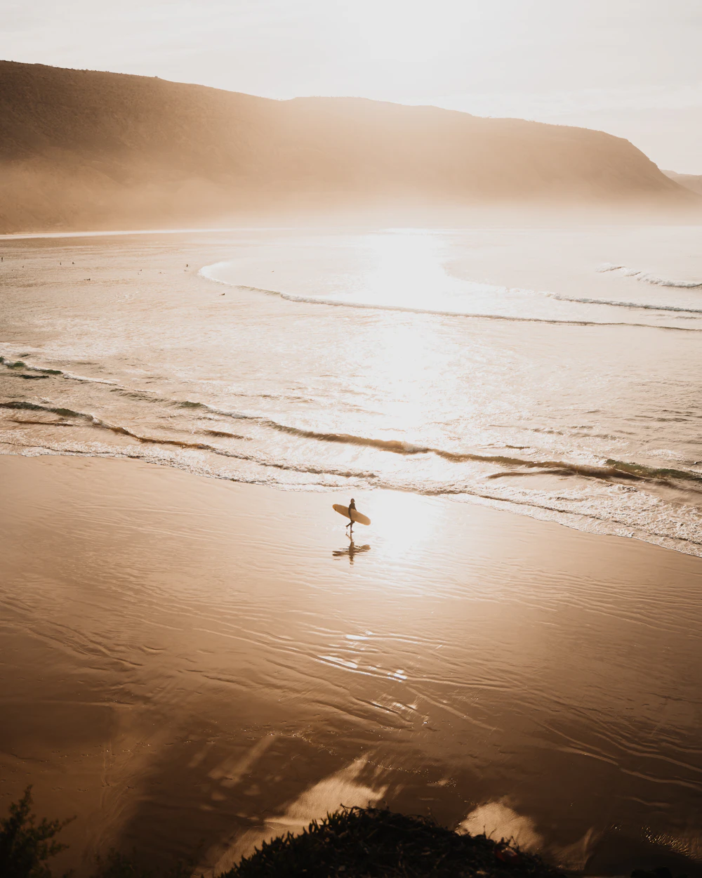 Person walking on a Moroccan beach with a surfboard.