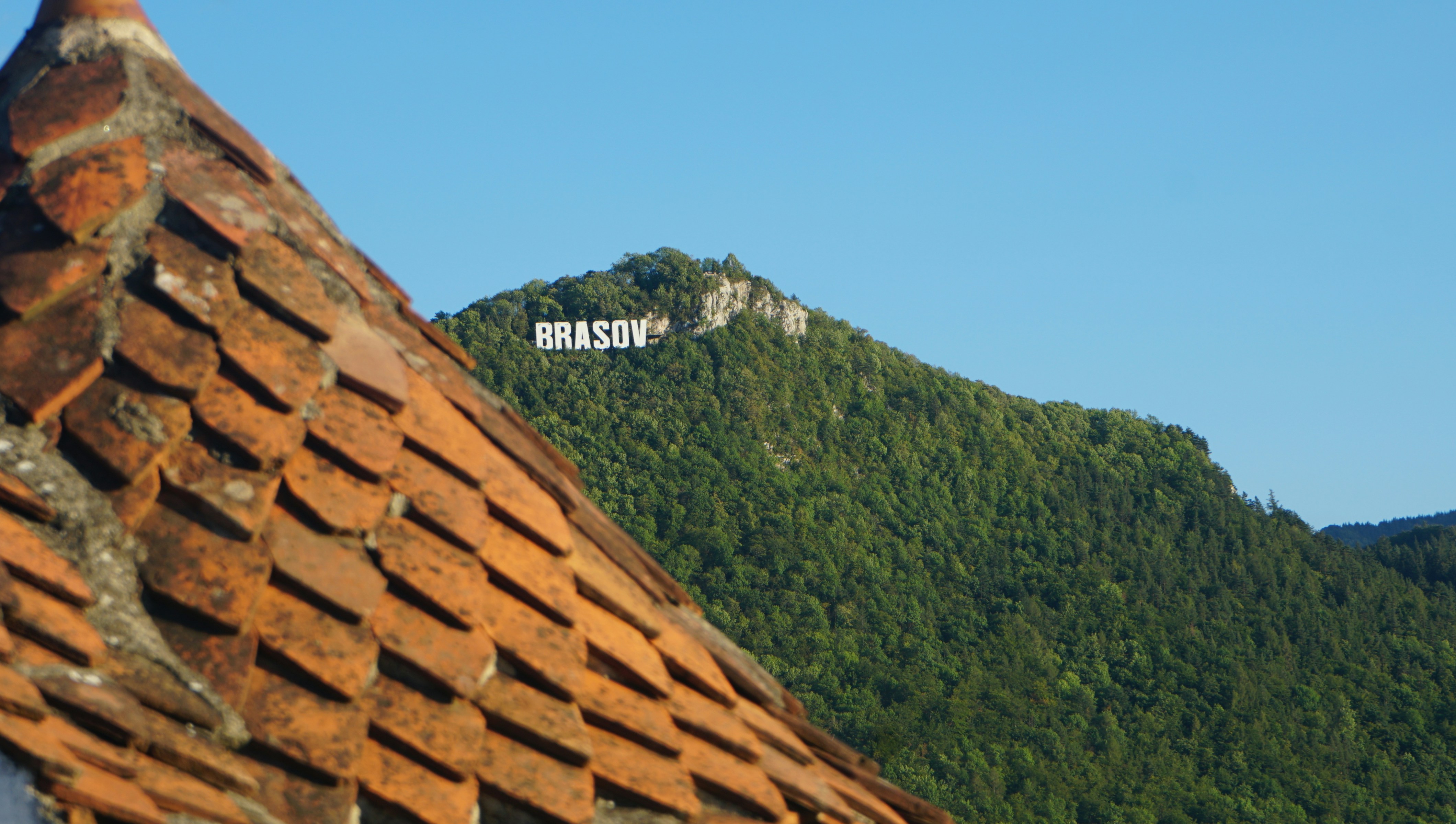 Brasov sign on mountain blue sky background roof tiles foreground