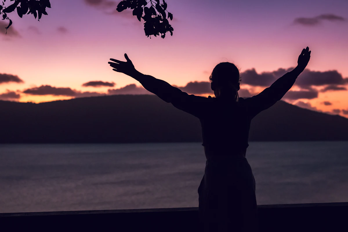 A person with arms open wide at sunset