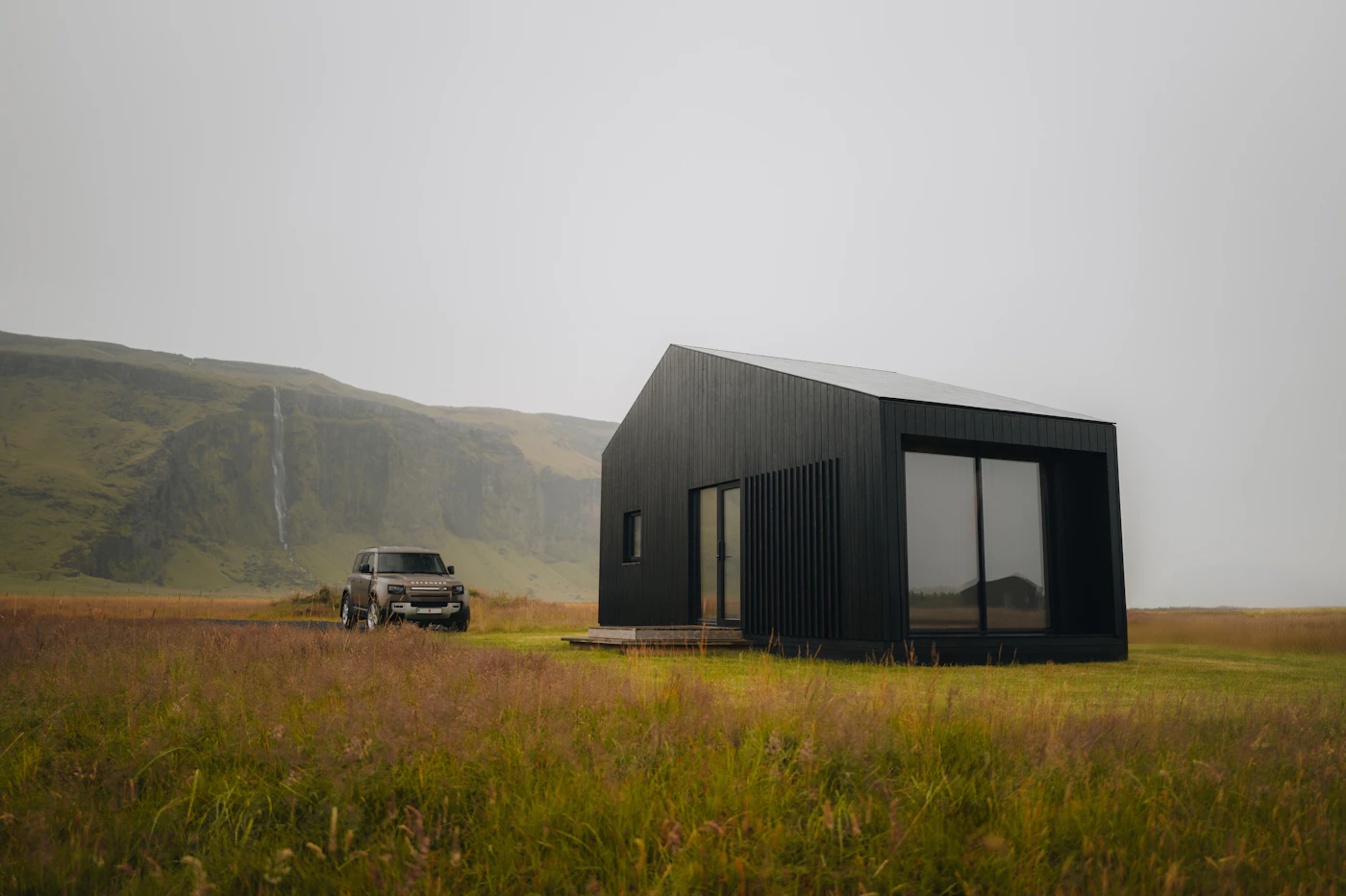Delivery truck parked beside a black prefab building in a field