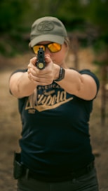 A woman with a hat and sunglasses aiming a gun
