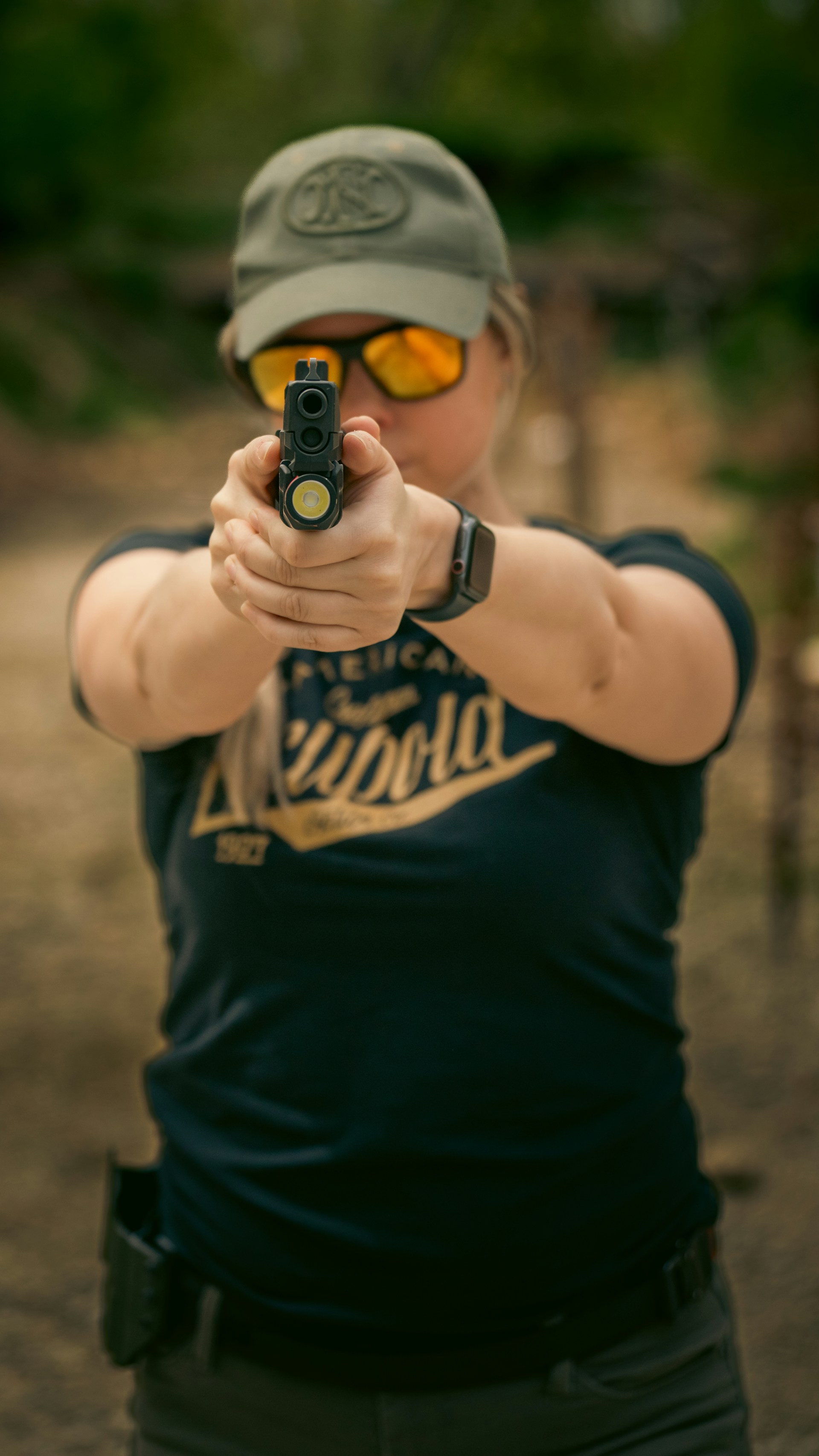 A woman with a hat and sunglasses aiming a gun