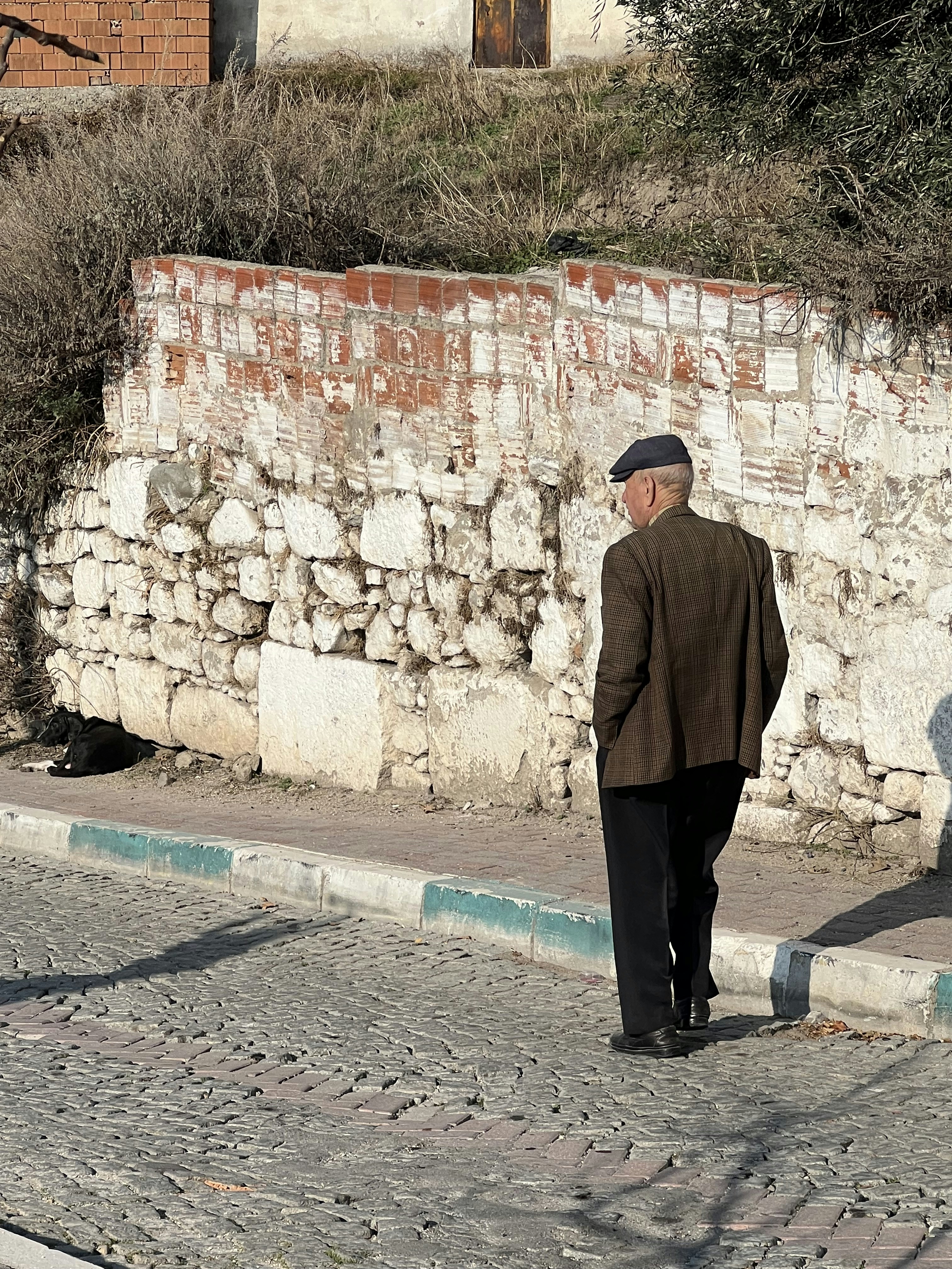 A man walking down a street next to a stone wall