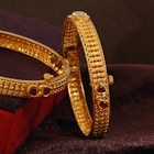 A pair of gold bracelets sitting on top of a velvet cushion