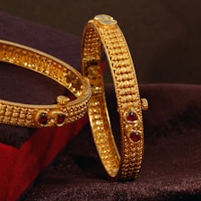 A pair of gold bracelets sitting on top of a velvet cushion