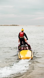 A man riding on the back of a yellow and black jet ski