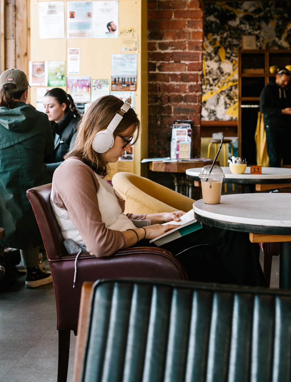 A woman in white headphones reads through her notes in an armchair at a busy café table