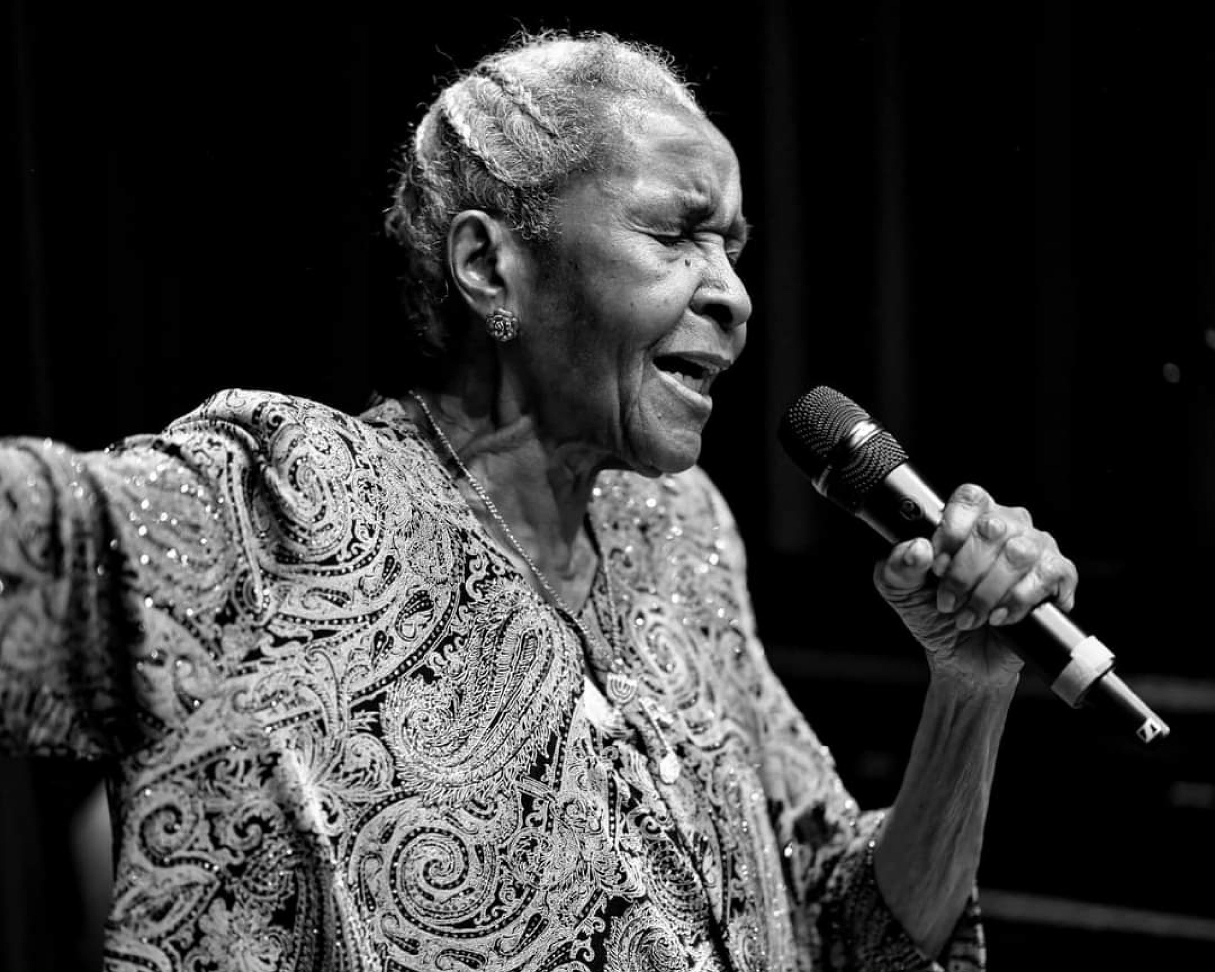 Una foto en blanco y negro de una mujer cantando en un micrófono
